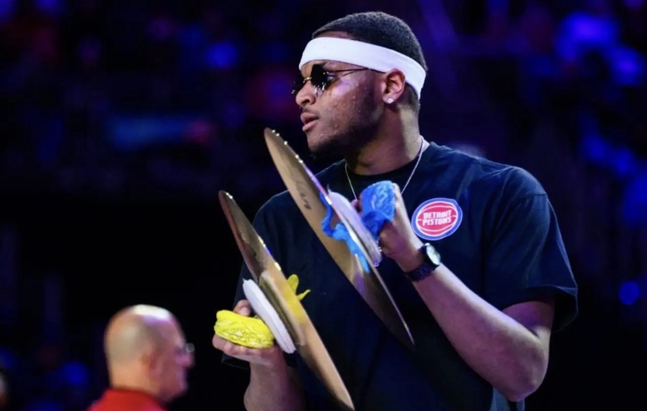 Person wearing sunglasses and a headband holding a trophy and medals, with a blurred background.