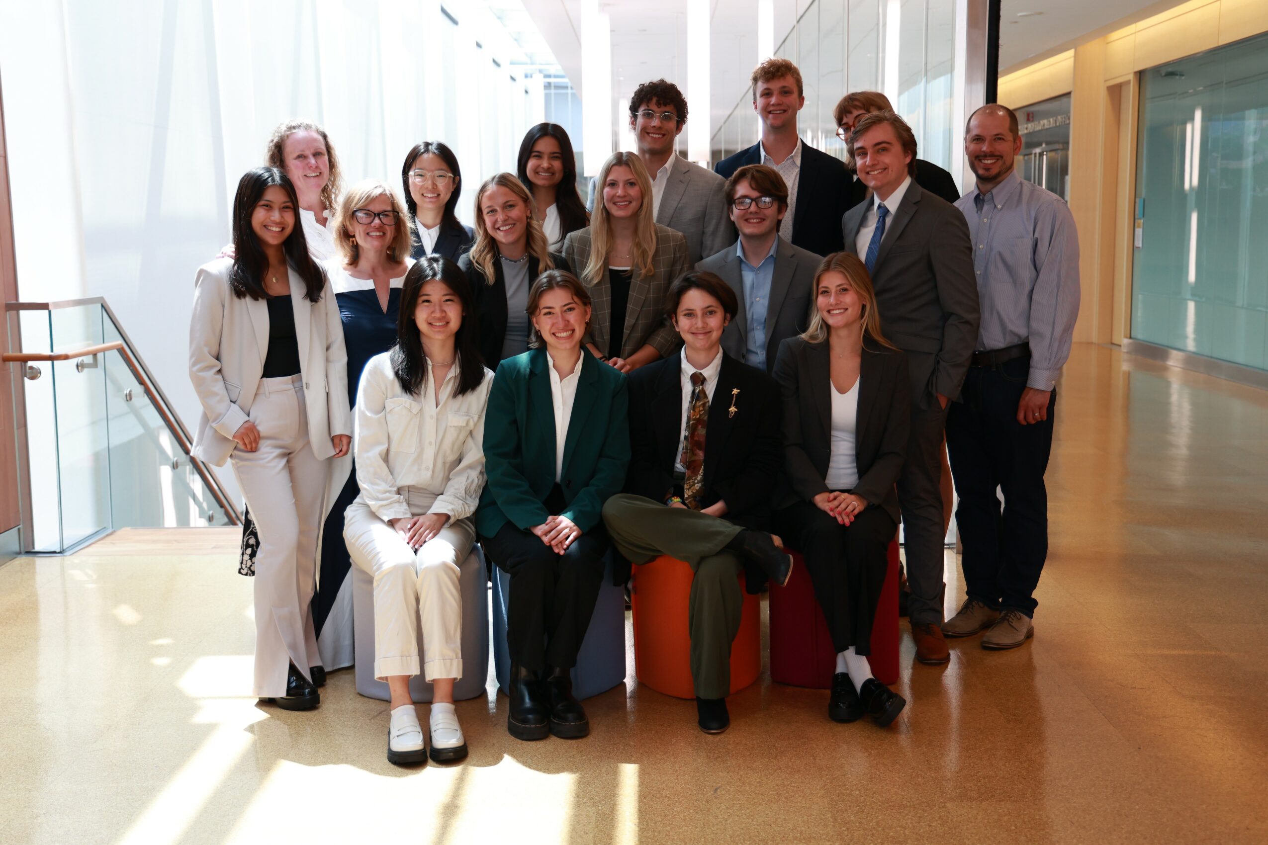 Group of 15 people in business attire posing indoors with large windows and natural light.