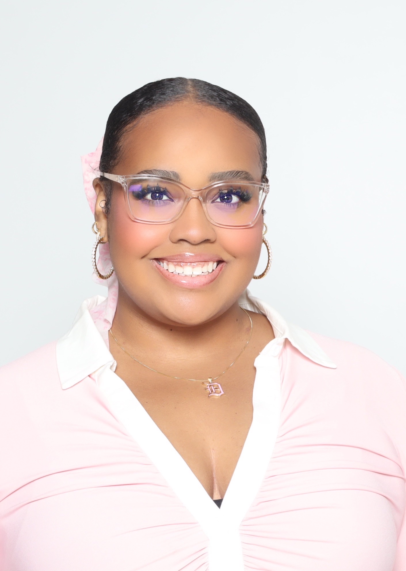 Smiling woman with glasses, earrings, and a necklace, wearing a light pink shirt, facing forward.