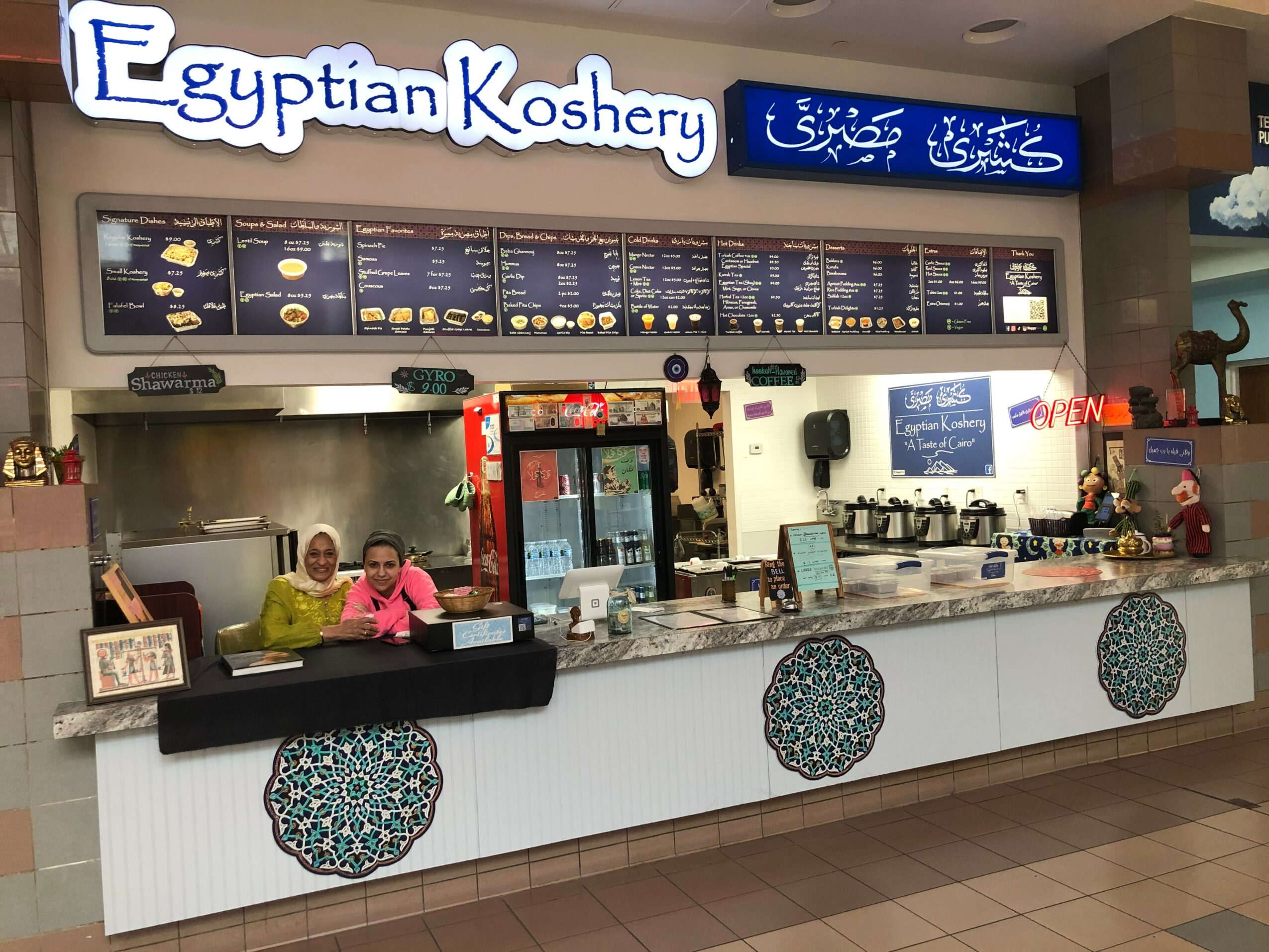 Counter service counter with menu boards, staff, and decorative tiles, sign reads 'Egyptian Koshery' in English and Arabic.