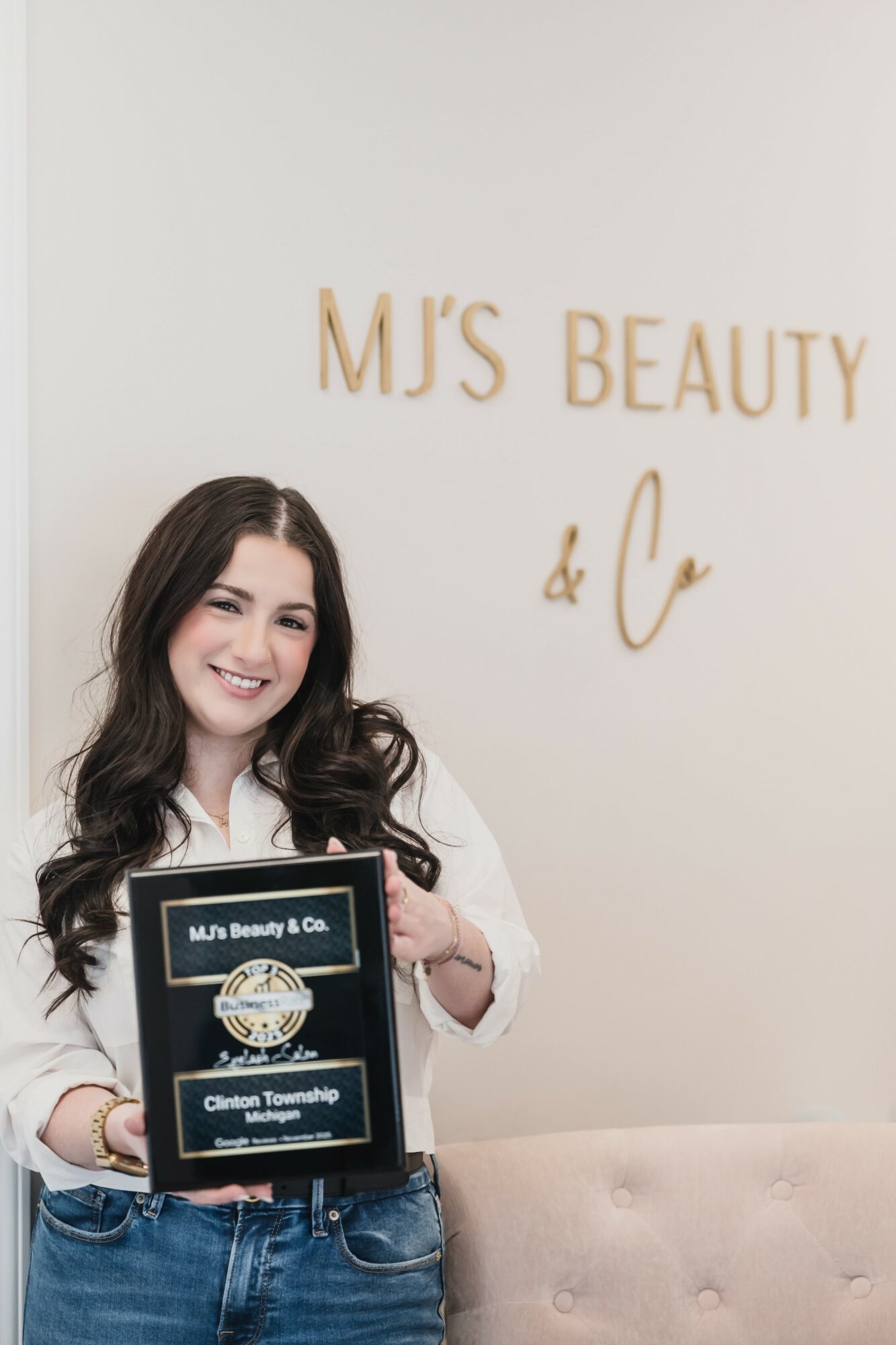 Smiling woman holding a framed certificate in front of a wall with gold lettering that reads