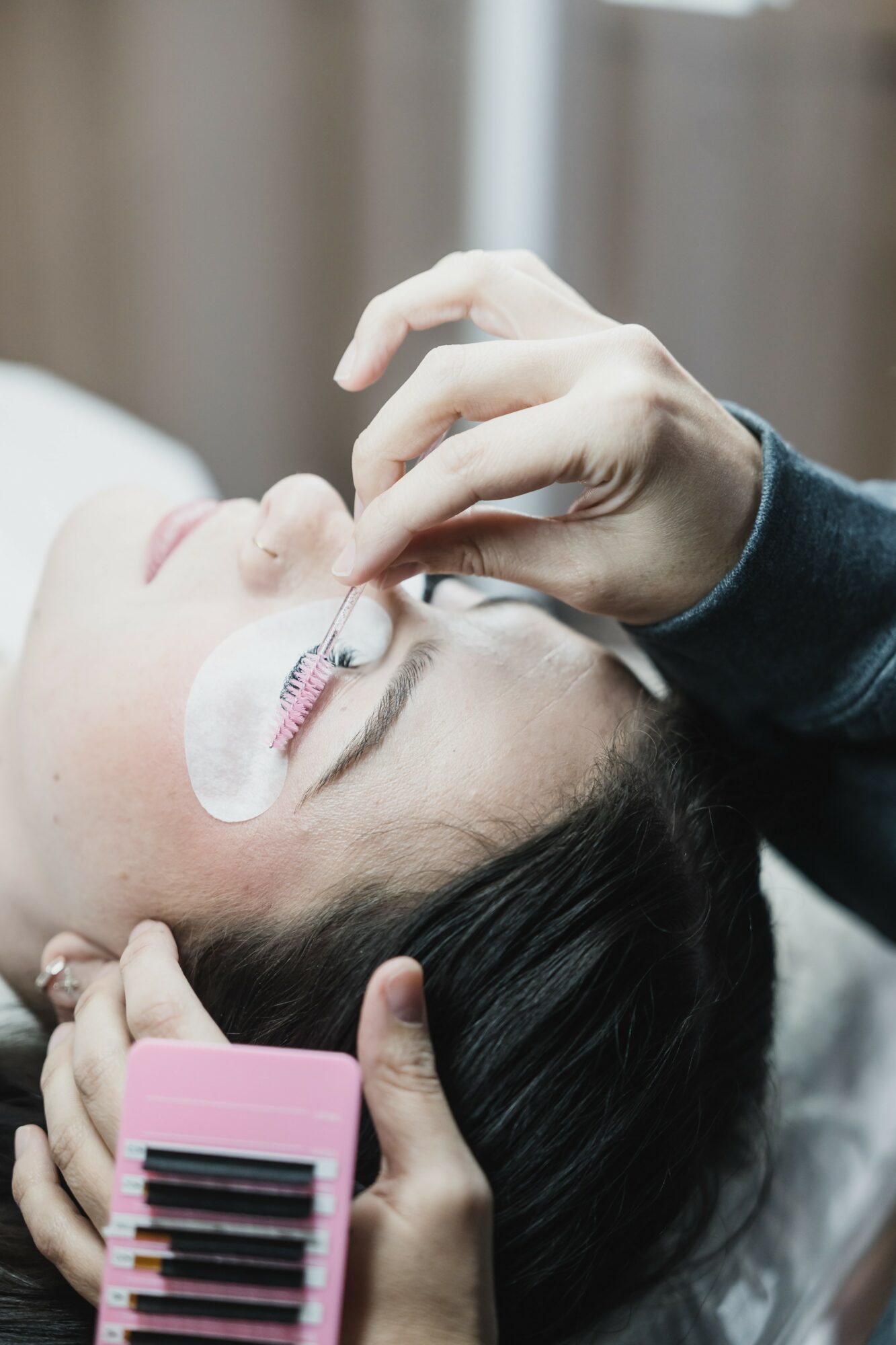 Person receiving a cosmetic procedure on their eye area, with a technician applying treatment and holding a pink device.