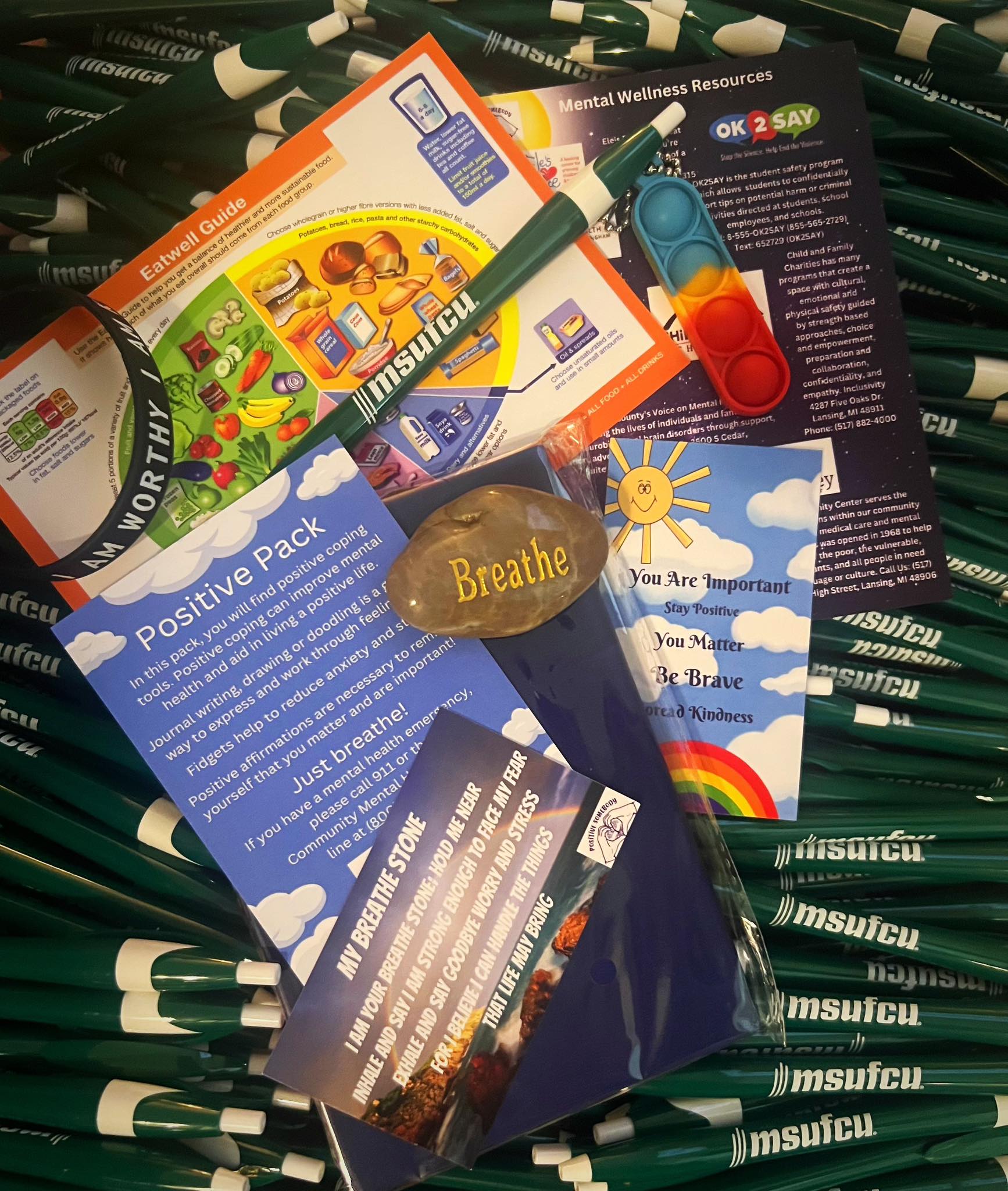 Collection of health and wellness brochures, a green pen, a blue inhaler, and a small stone with the word 'Breathe' on it, surrounded by black and white pens.