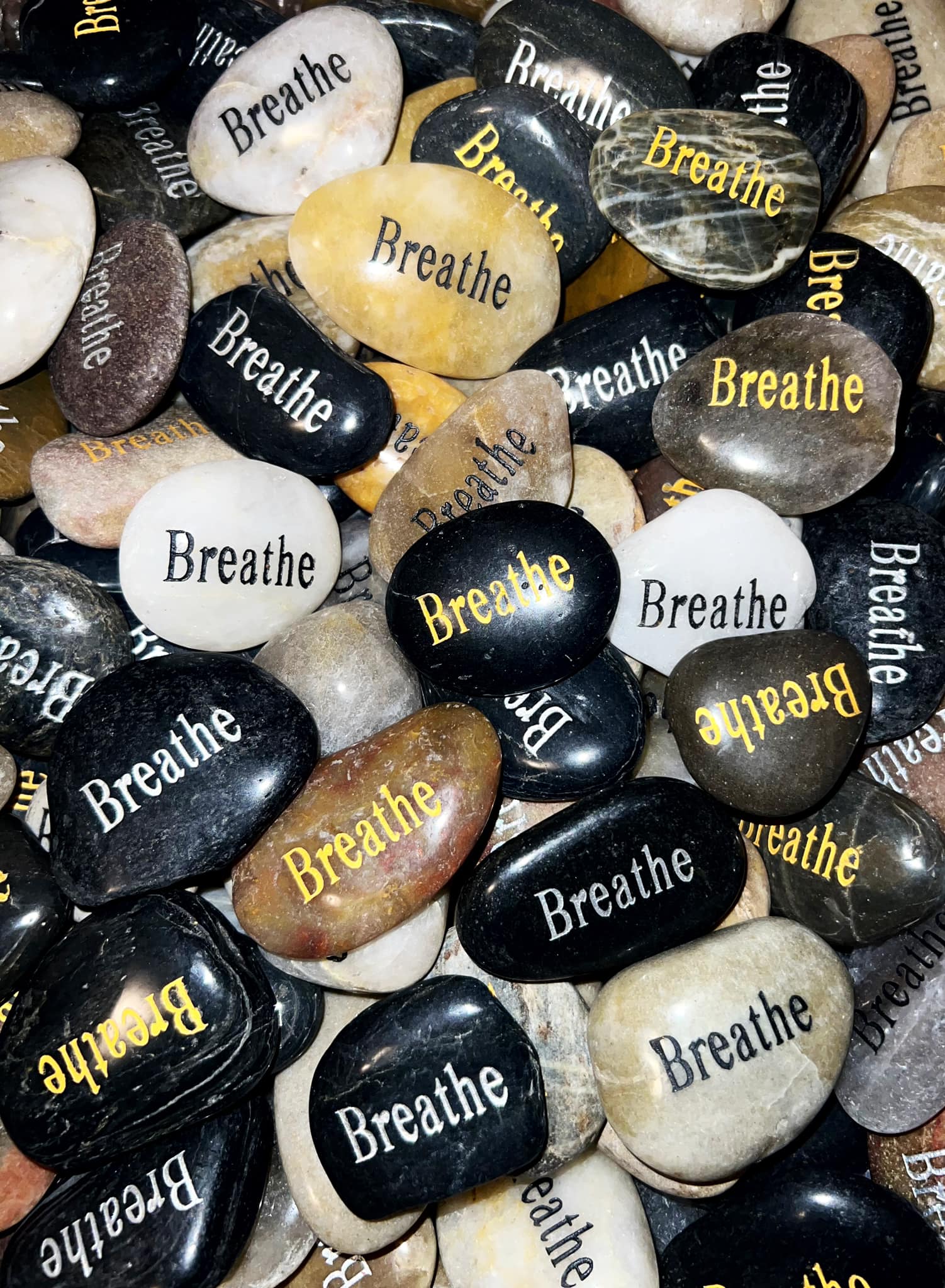 A collection of smooth stones with the word 'Breathe' in various colors and fonts, arranged randomly.