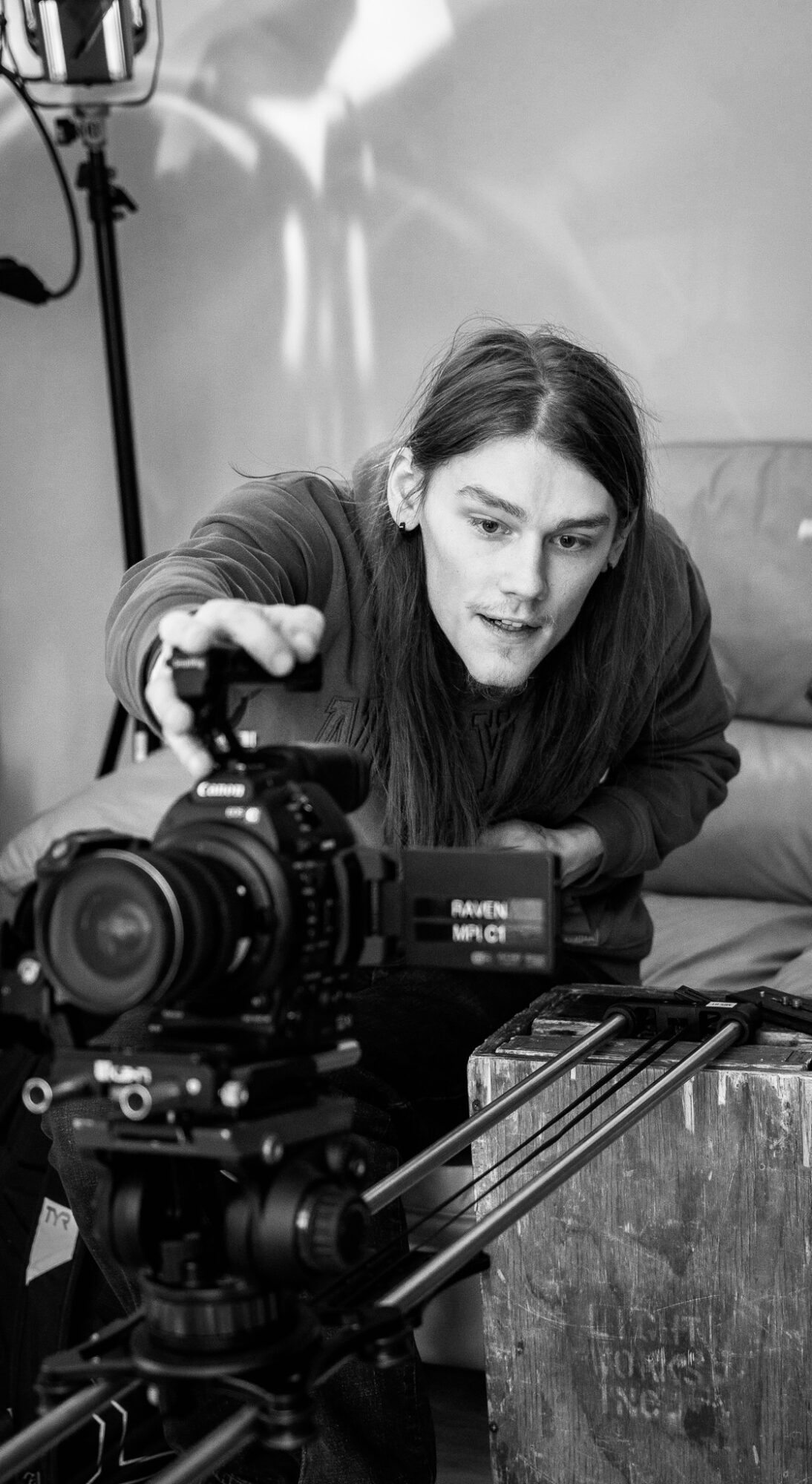Woman operating a camera, looking at the viewfinder, with equipment on a table in front of her.