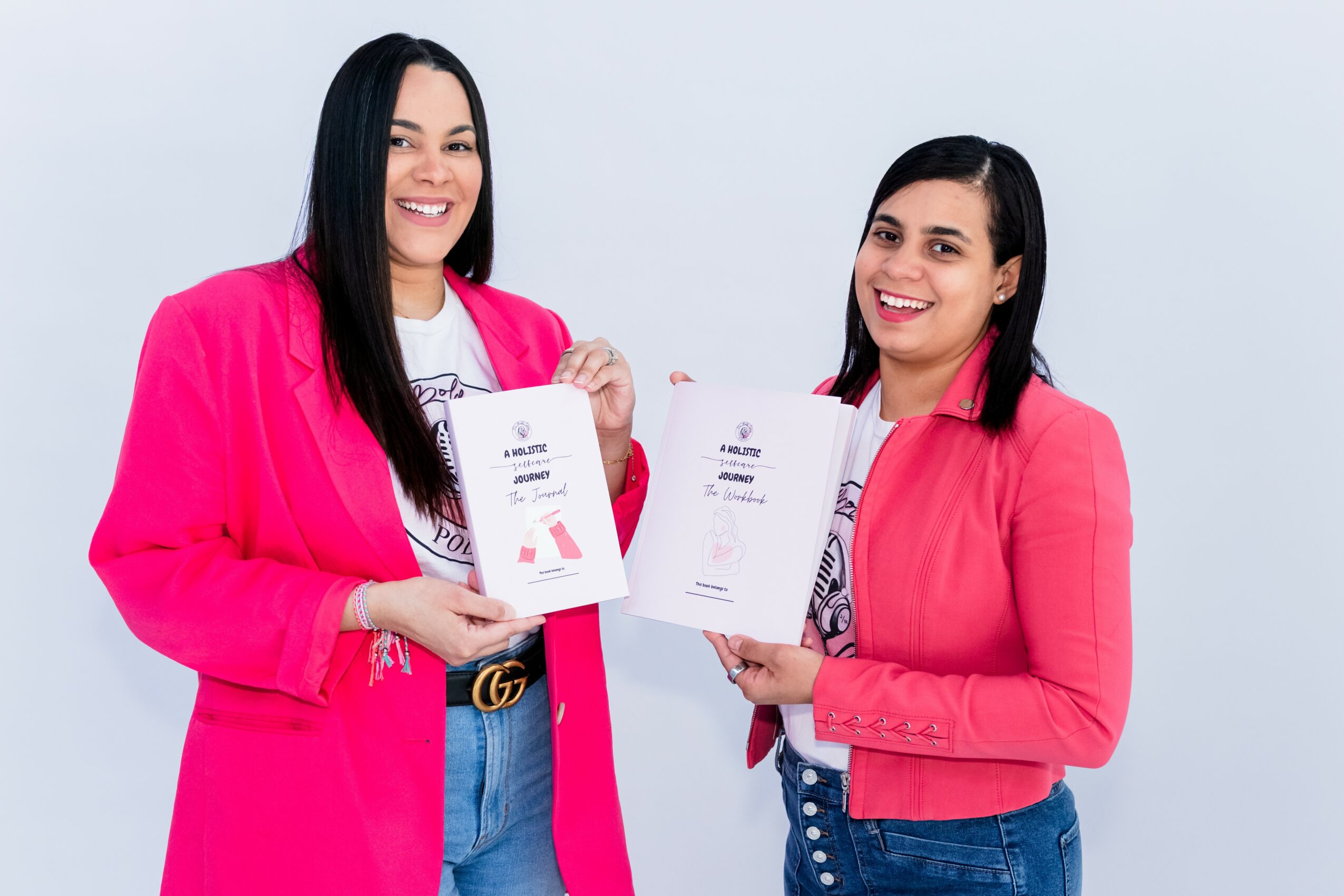 Two women in pink blazers holding documents and smiling, standing against a light background.