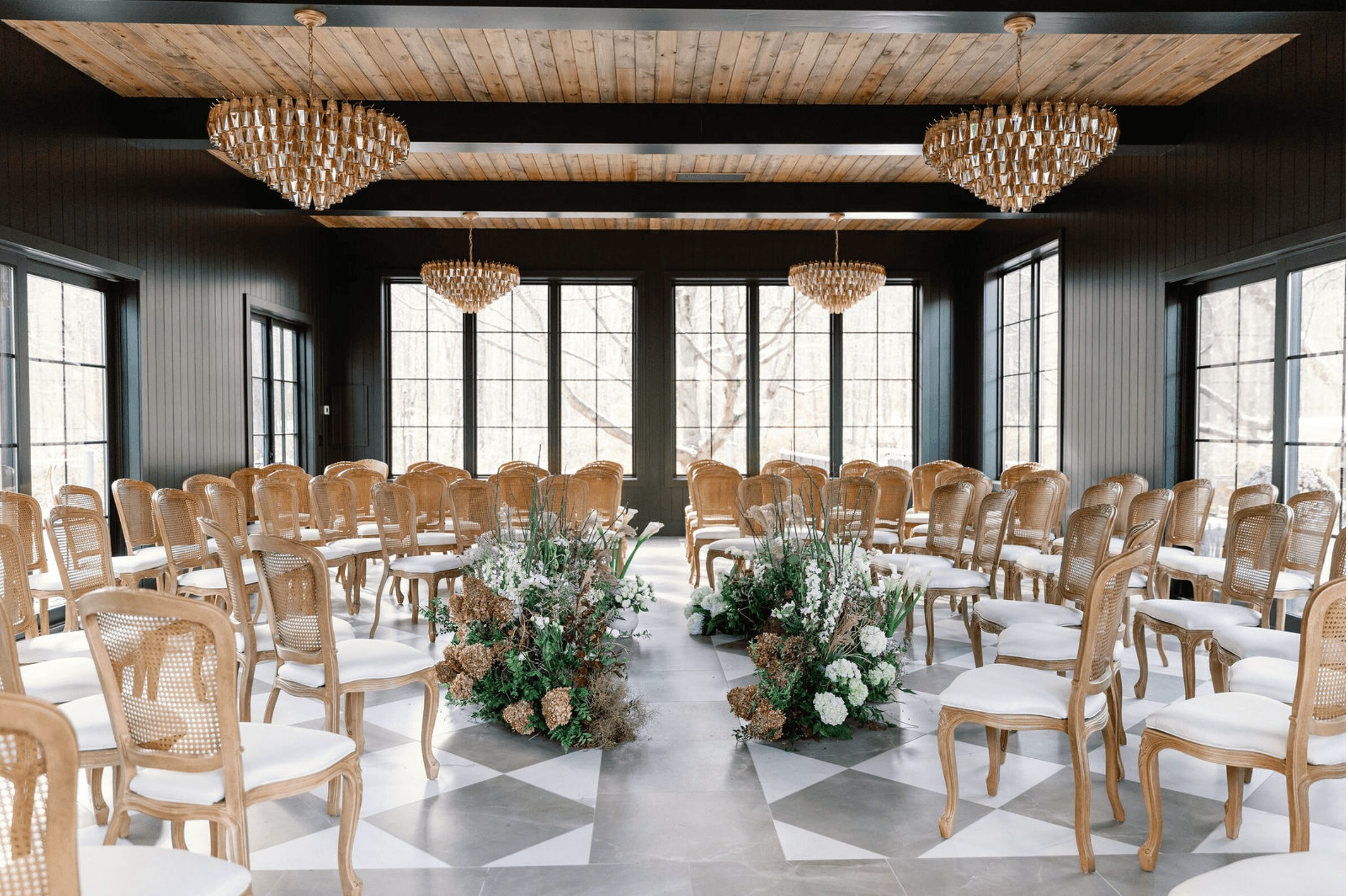 Elegant event space with rows of chairs, floral arrangements, large windows, and chandeliers, ready for a gathering.