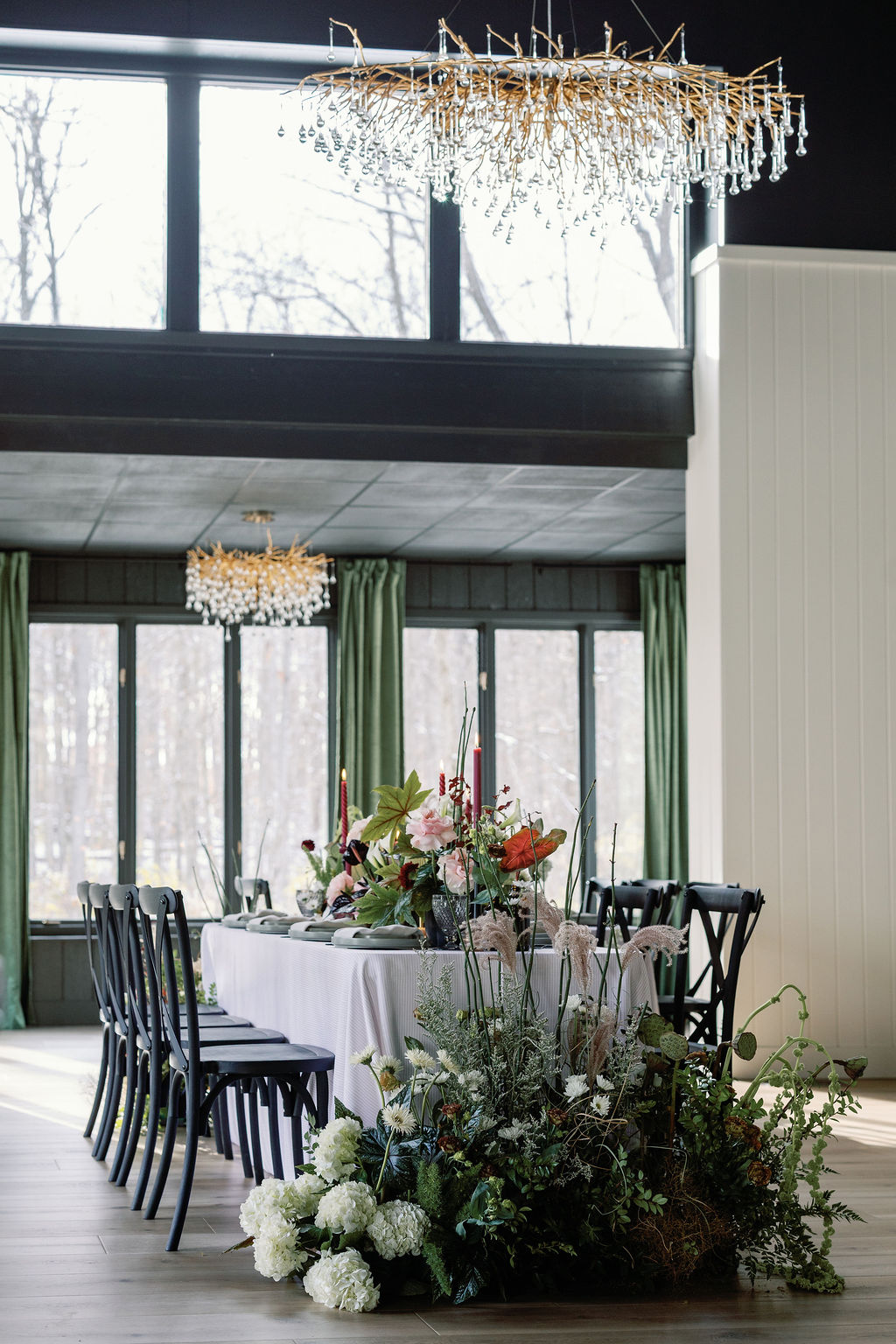 Elegant dining room with large windows, green curtains, a round table with floral centerpiece, and black chairs, decorated for an event.