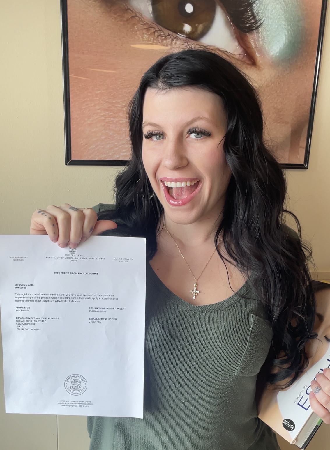 Woman with long dark hair smiling and holding a document, standing in front of a large eye artwork.