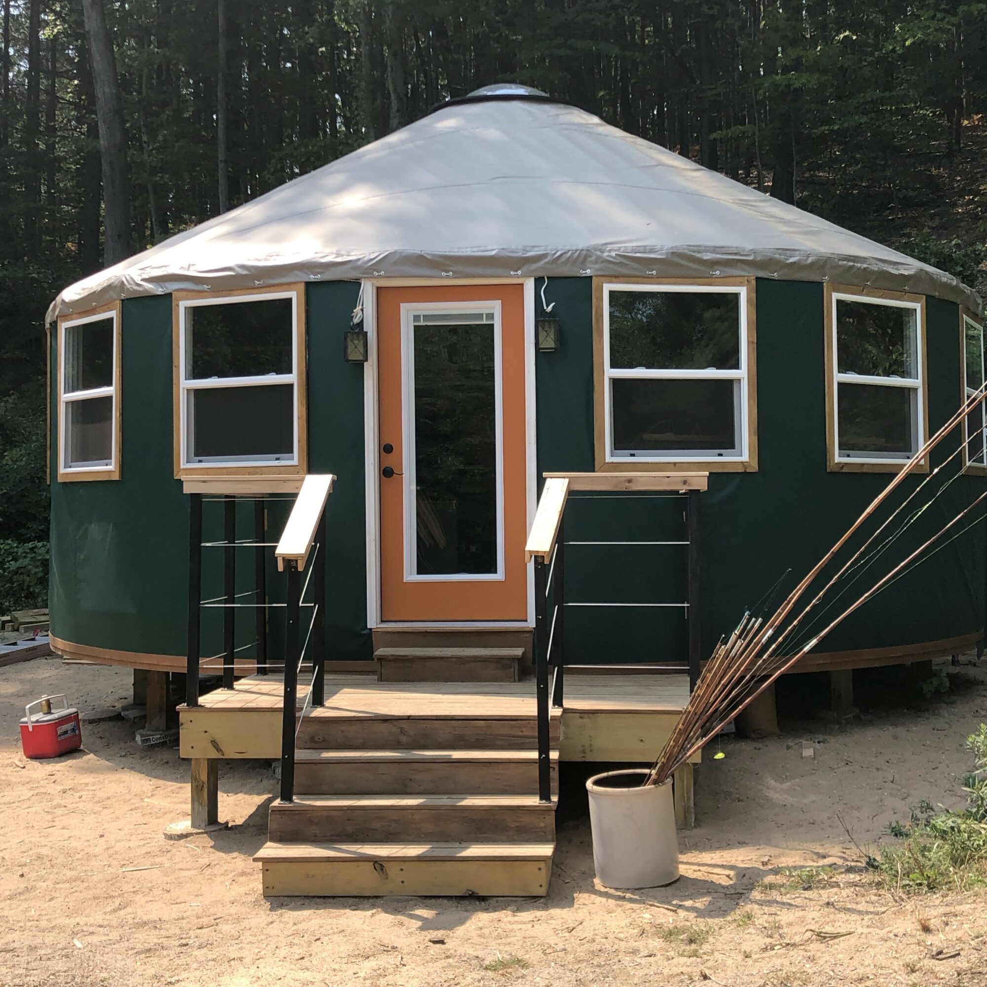 Round tent with a central door, multiple windows, and a small staircase, set outdoors with trees in the background.
