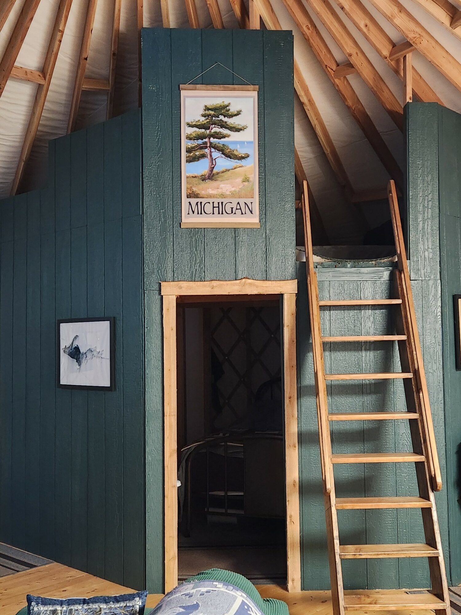 Interior of a wooden attic with green walls, a ladder leading to a small upper area, and framed artwork on the wall.