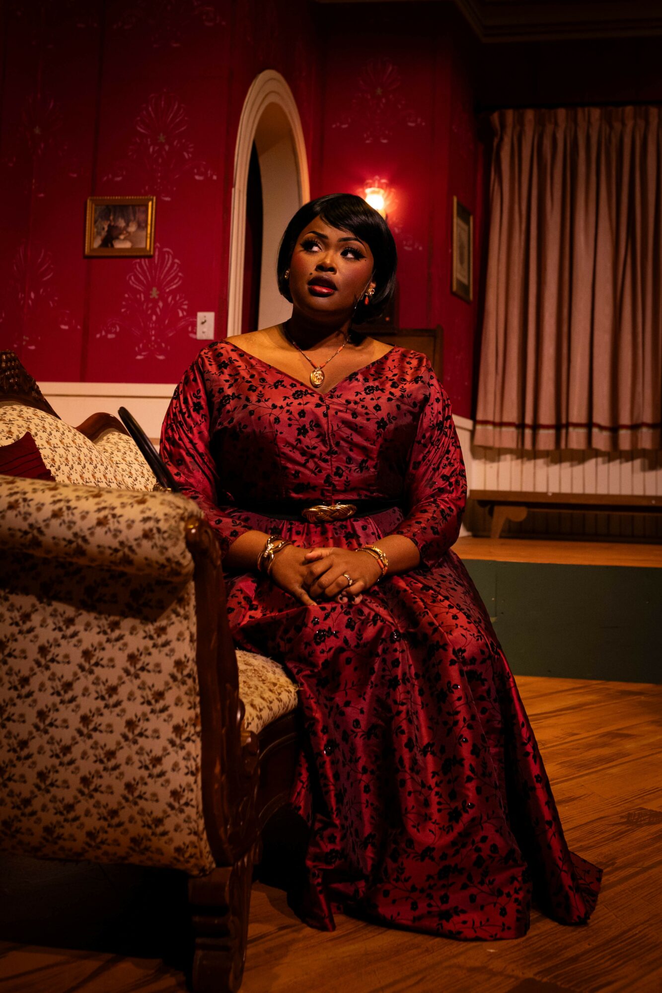 Woman in red dress sitting on a sofa in a room with red walls and curtains.