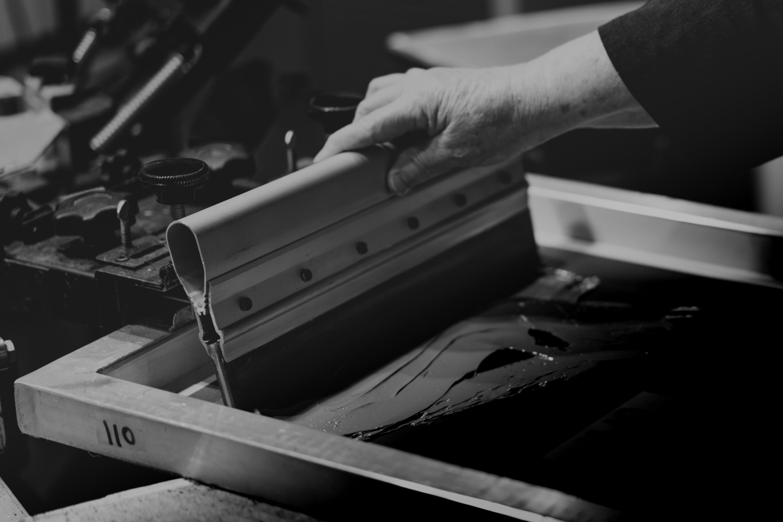 Person's hand flipping through a binder with papers, on a cluttered desk, in black and white.