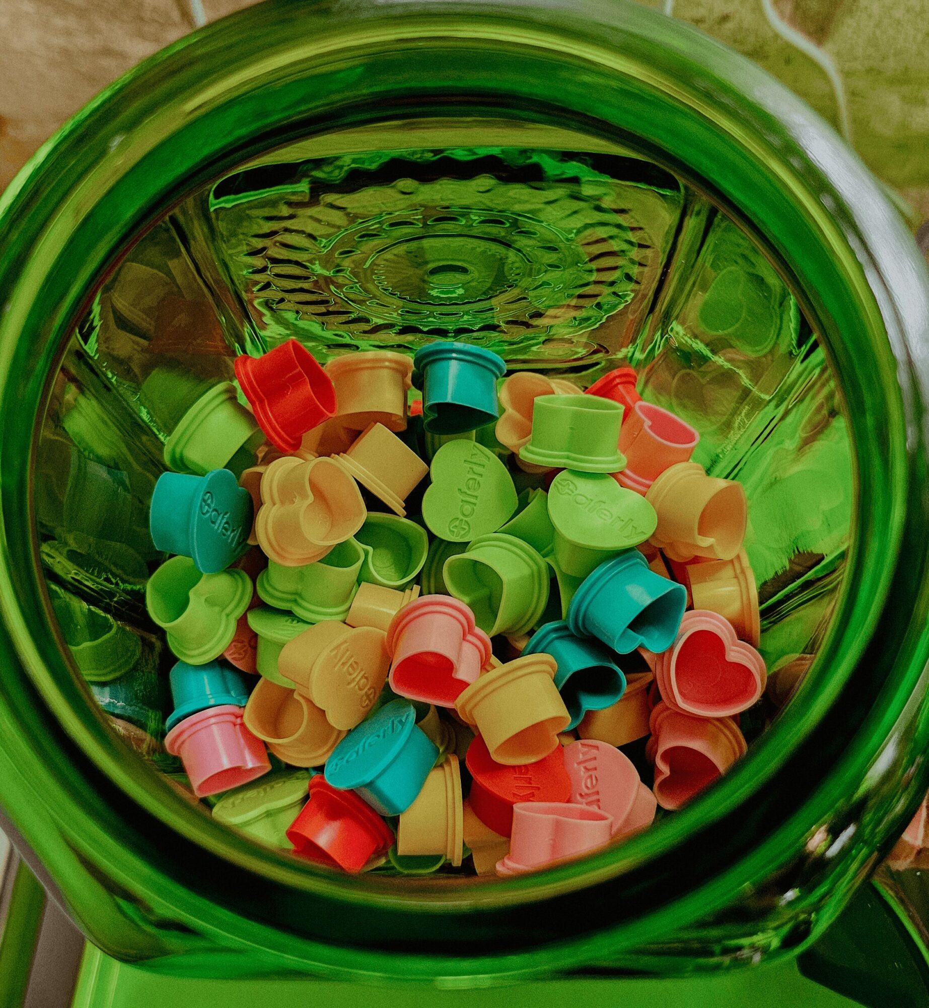 View from above into a green container filled with colorful plastic caps in various shapes and colors.