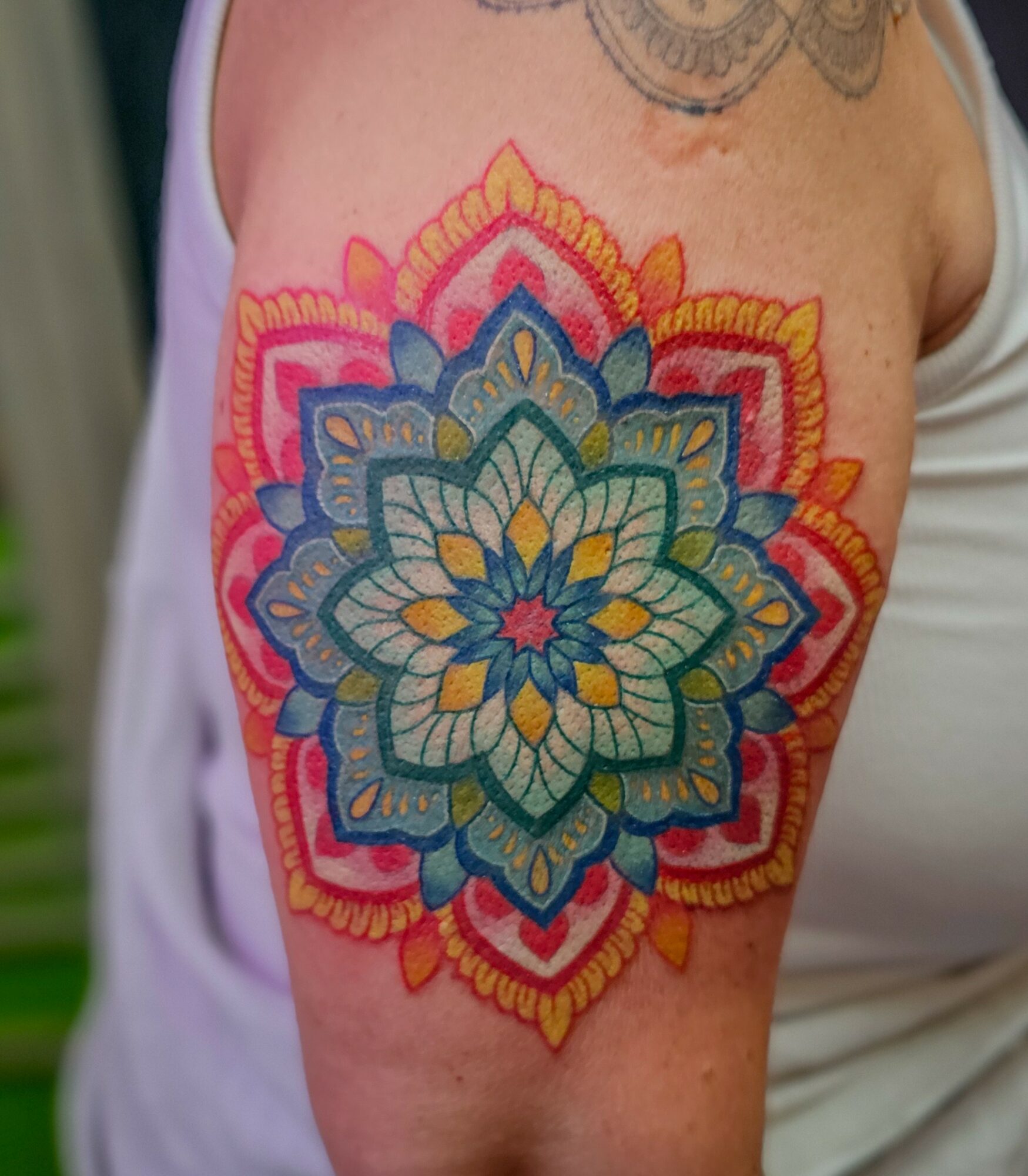 Colorful mandala tattoo on upper arm with intricate patterns and vibrant colors, including blue, yellow, pink, and orange.