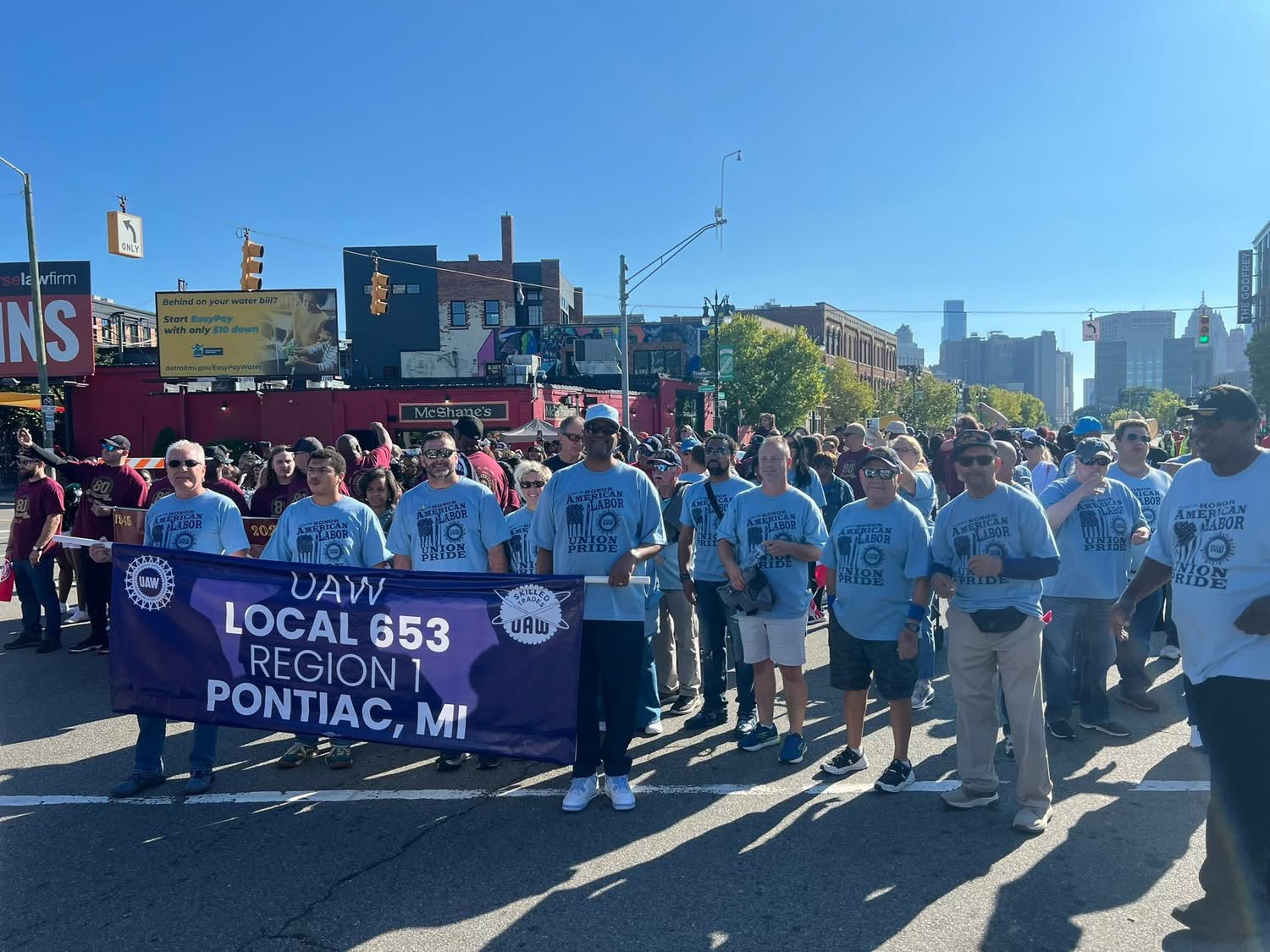 Group of people holding a banner that reads 'UAW Local 653, Region 1, Pontiac, MI' outdoors on a sunny day.