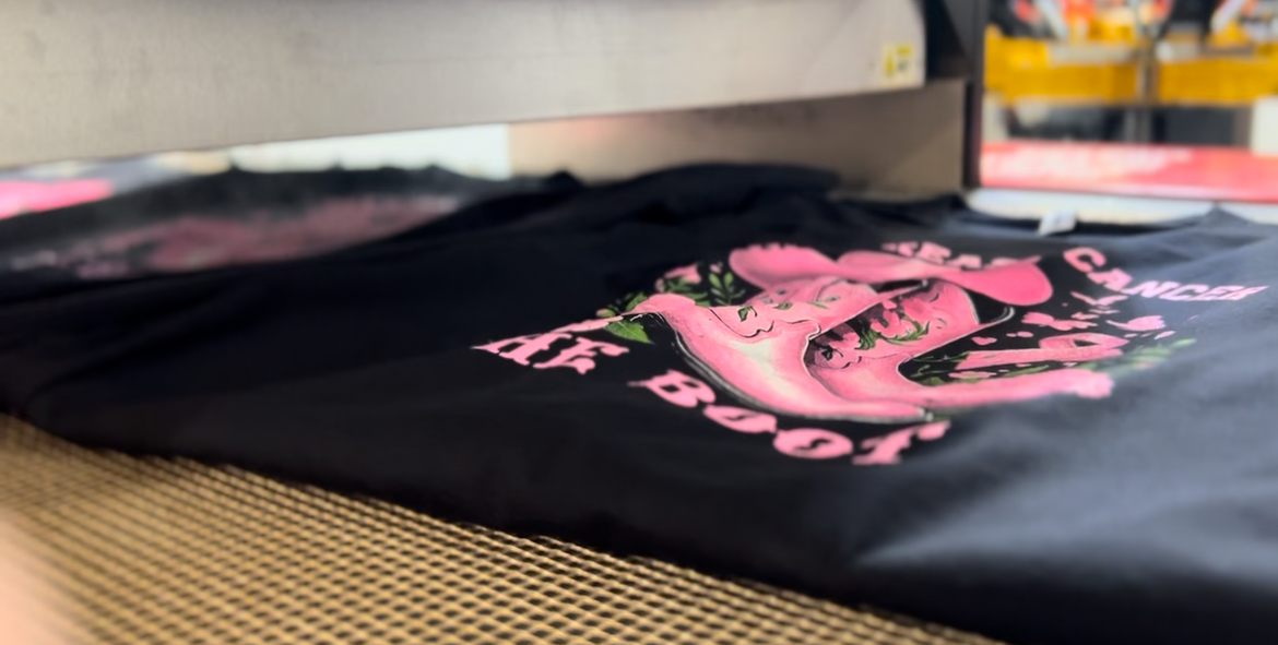 Black fabric with pink and white graphic design, laid on a textured surface, with a blurred background.
