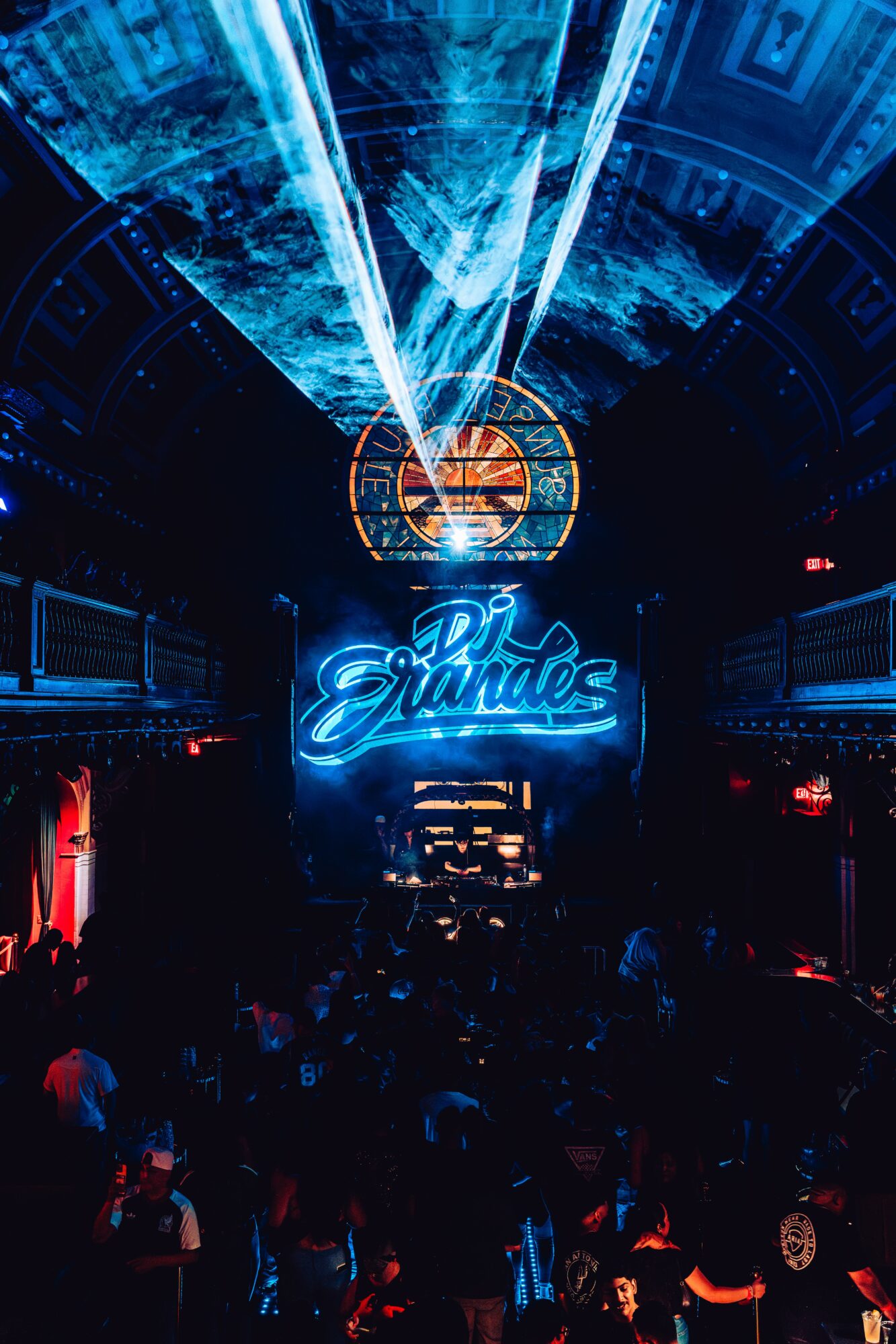 Crowd in a nightclub with blue neon sign reading 'Elounda' and laser lights overhead, dark atmosphere.