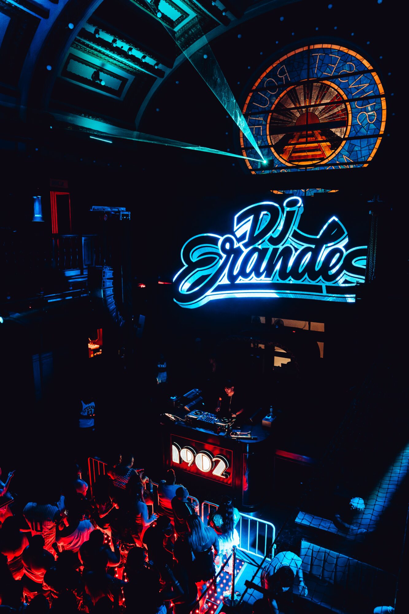 DJ performing on stage with a neon sign reading 'DJ Tande,' audience in front, illuminated by colorful lights.