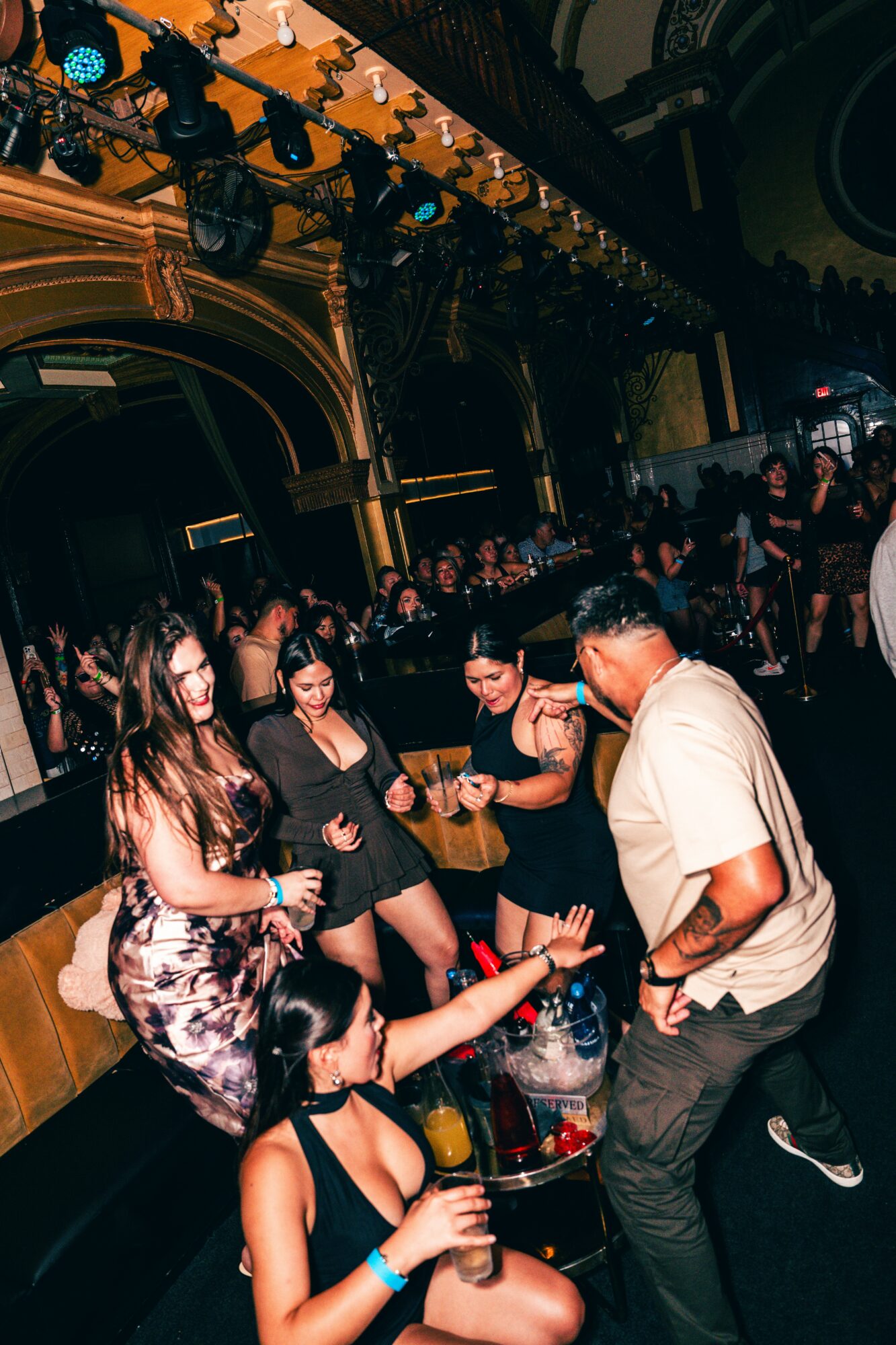Group of people dancing and socializing in a dimly lit, ornate venue with gold accents and high ceilings.