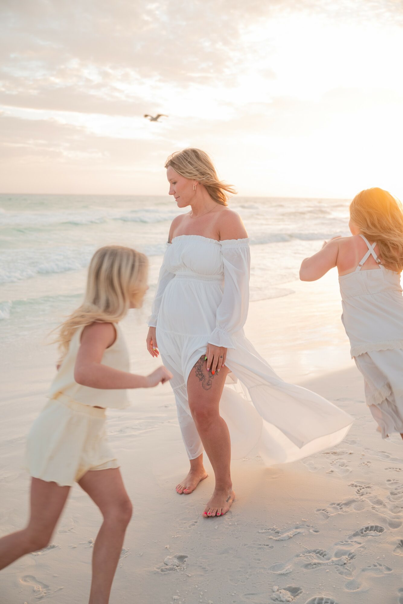 Woman and two children on the beach, holding hands, with ocean and sky in background.