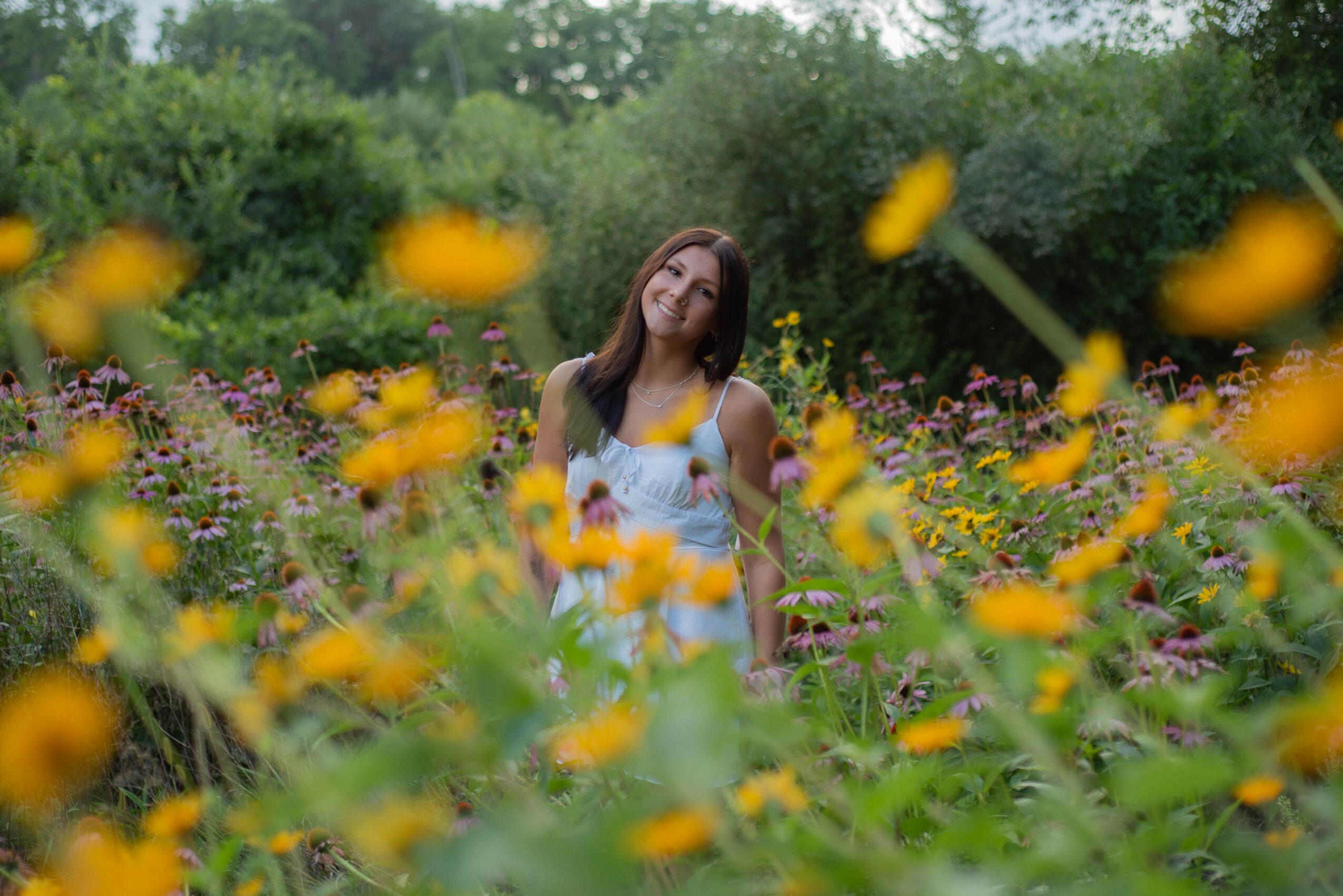 Young woman standing in a colorful flower field with green trees in the background.