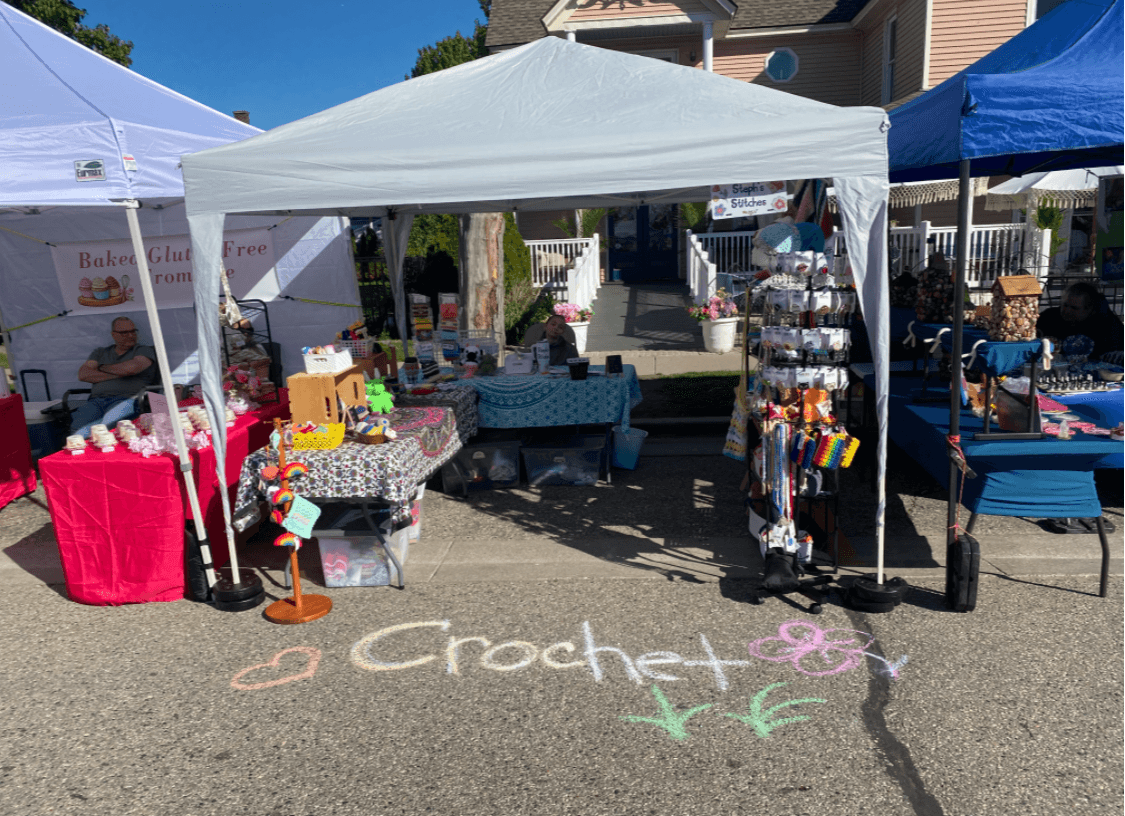 Outdoor craft booth with tables, tents, and colorful items, with chalk writing on pavement reading 'Crafts' and hearts.