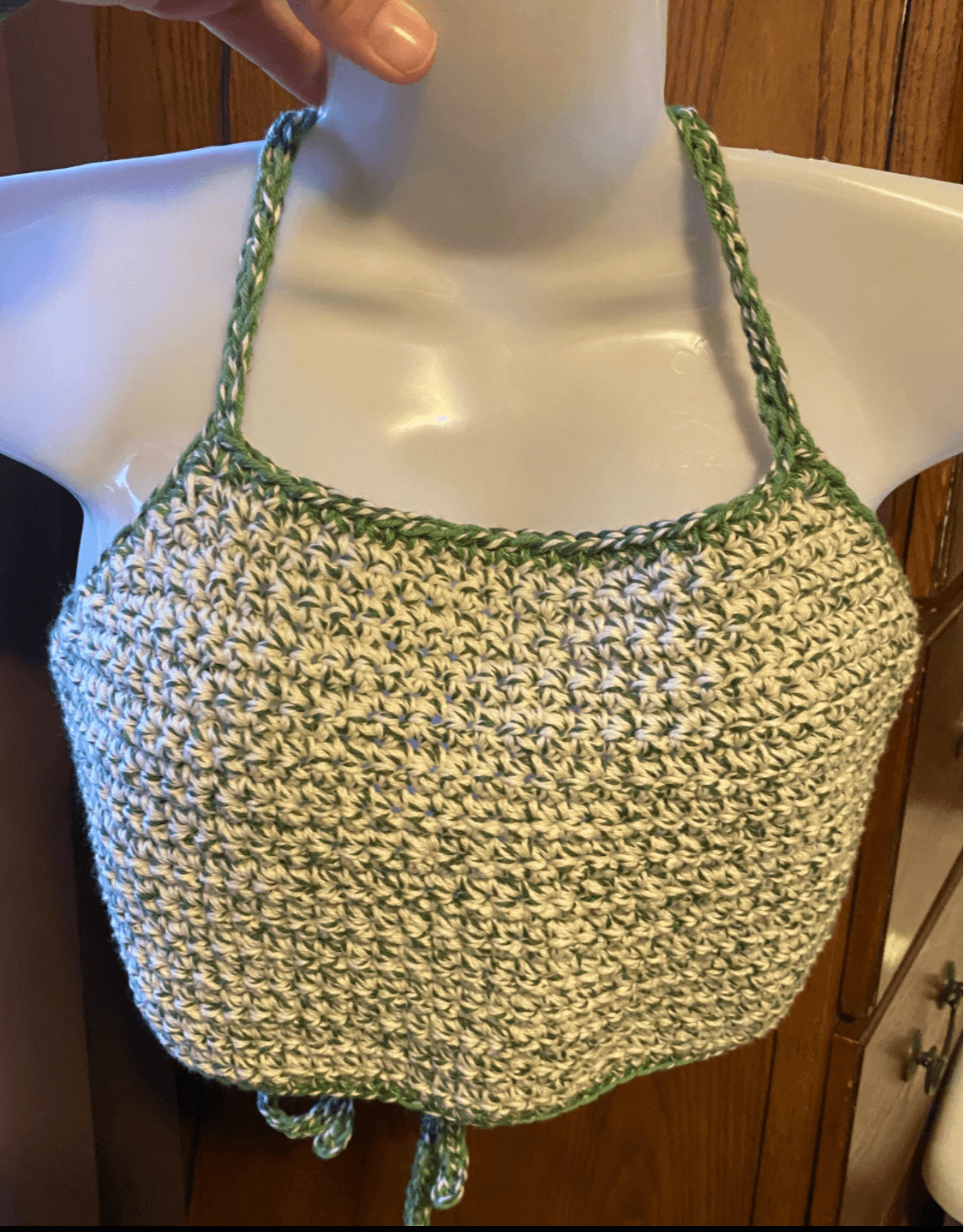 Crocheted halter top with green trim displayed on a mannequin, with a wooden background.