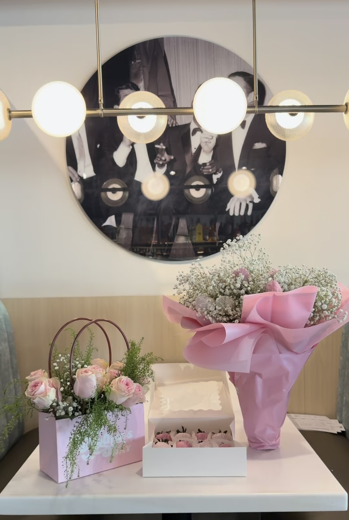 Round mirror reflecting people in formal attire, hanging light fixture, and a table with flower arrangements.