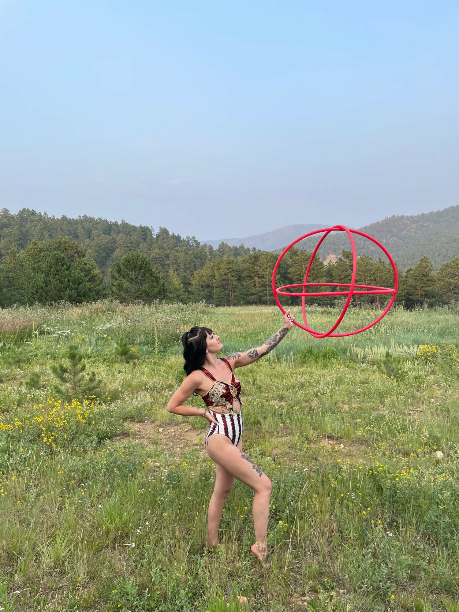 Person in striped swimsuit lying on grass near a red geometric structure, with green fields and trees in the background.