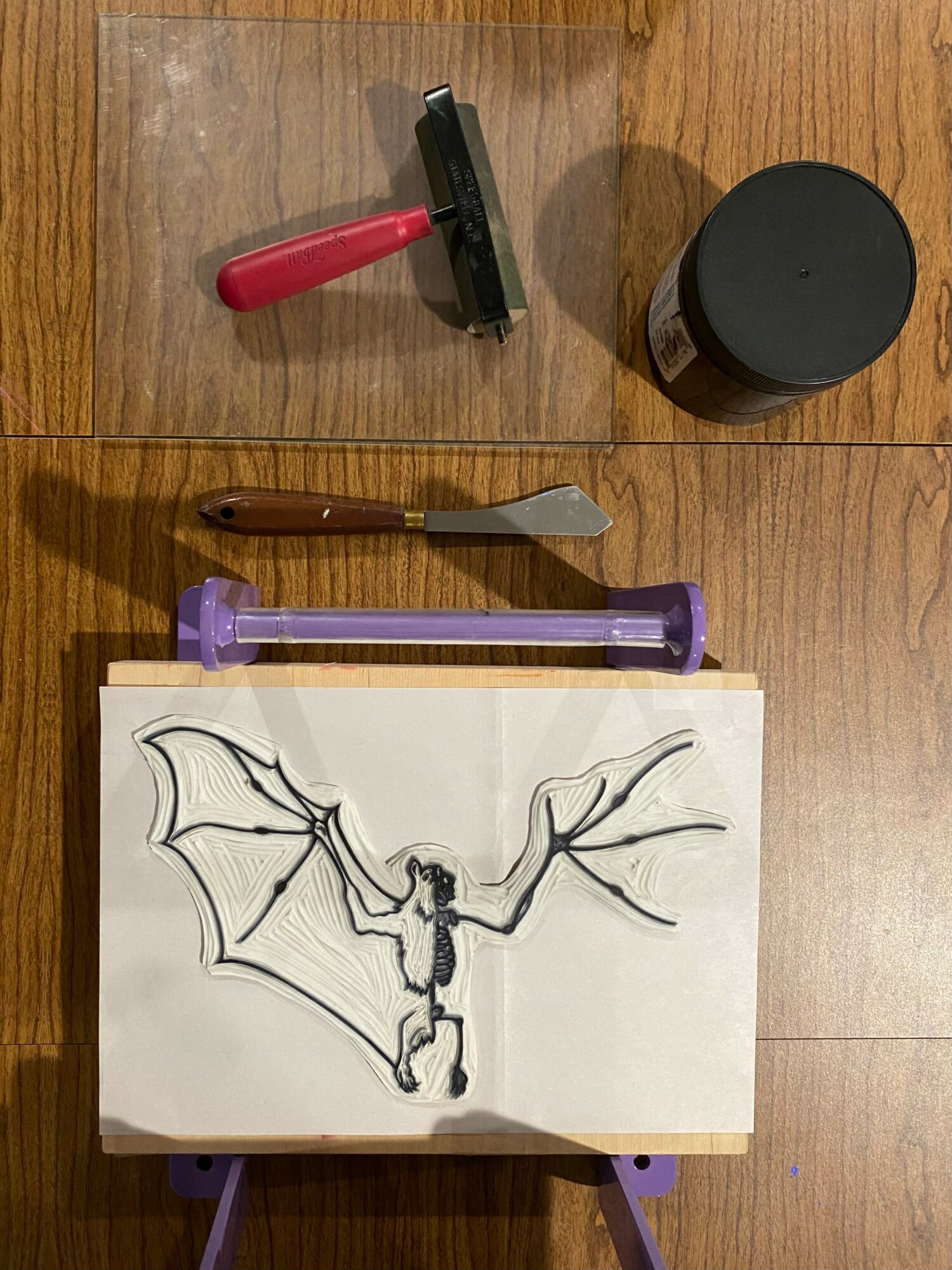 Drawing of a bat-like creature with large wings and a humanoid body on paper, placed on a wooden surface.