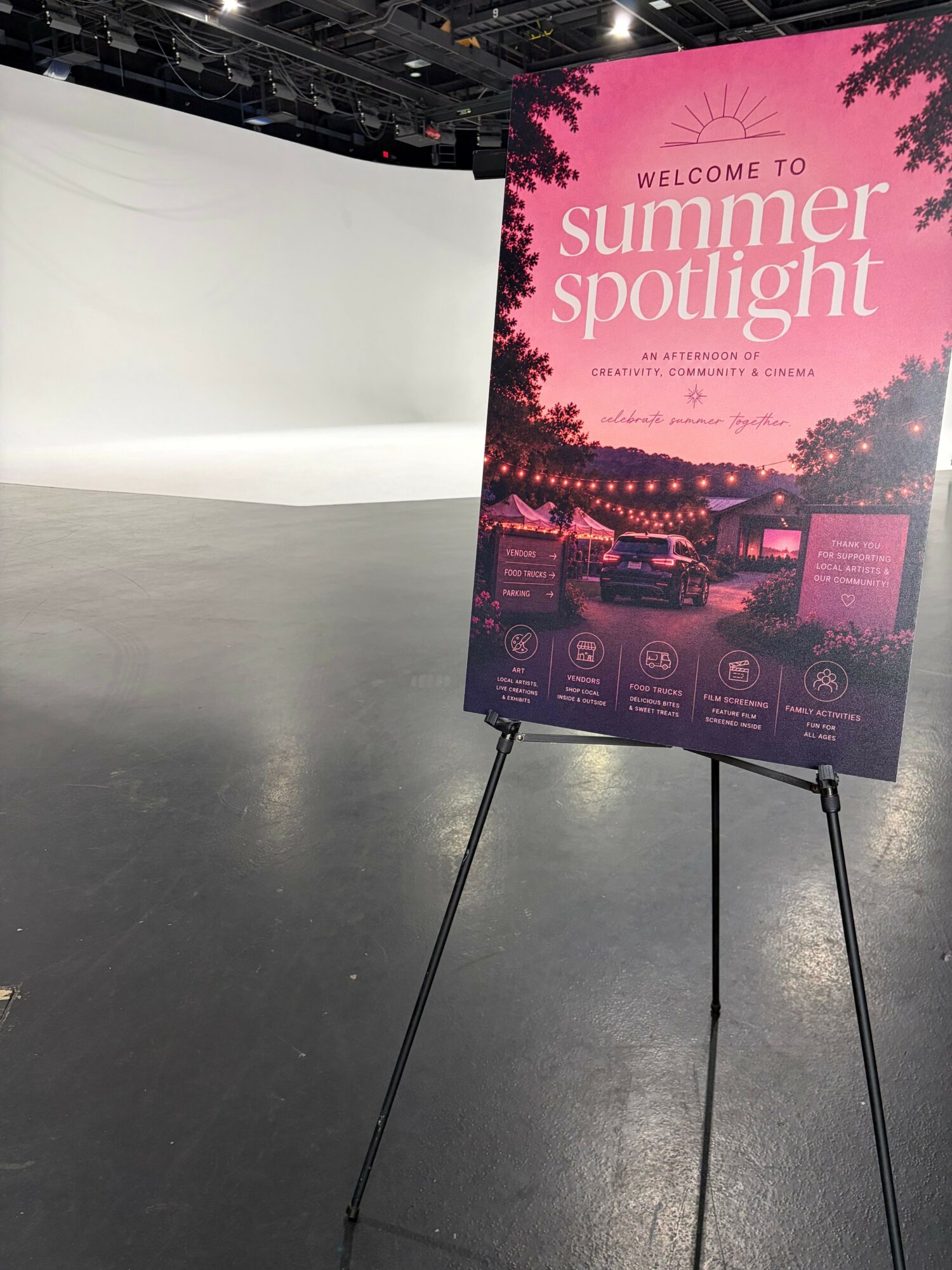 Signboard advertising summer night event, with pink and purple colors, on a wet surface, with a body of water in the background.