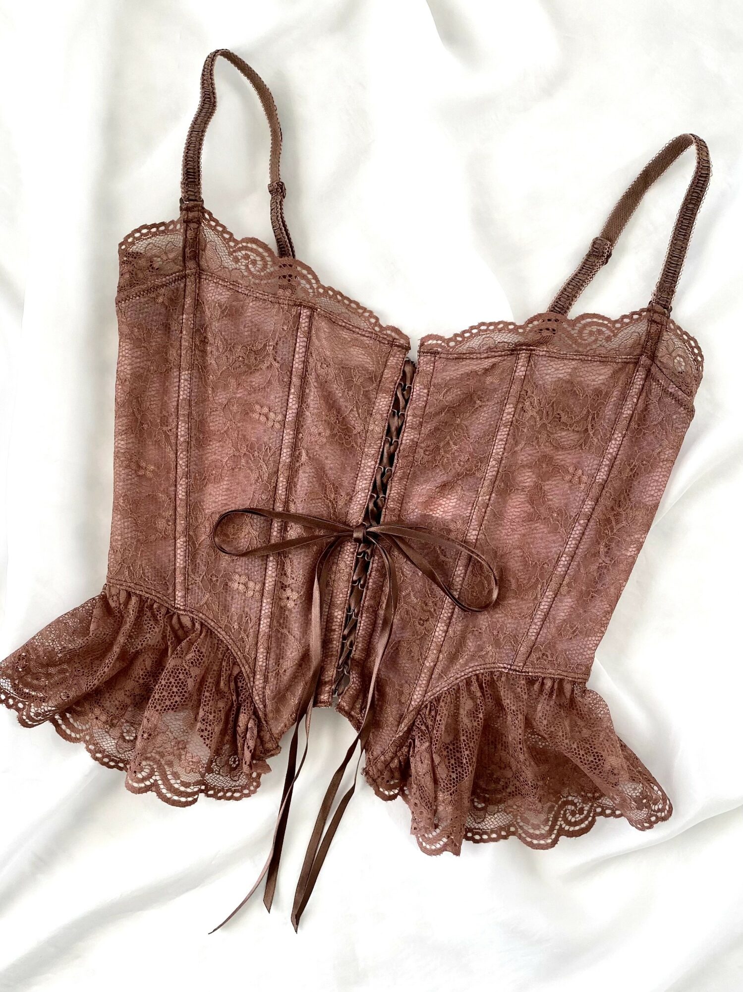 Brown lace corset with ruffled edges and a front tie, laid on a white fabric background.