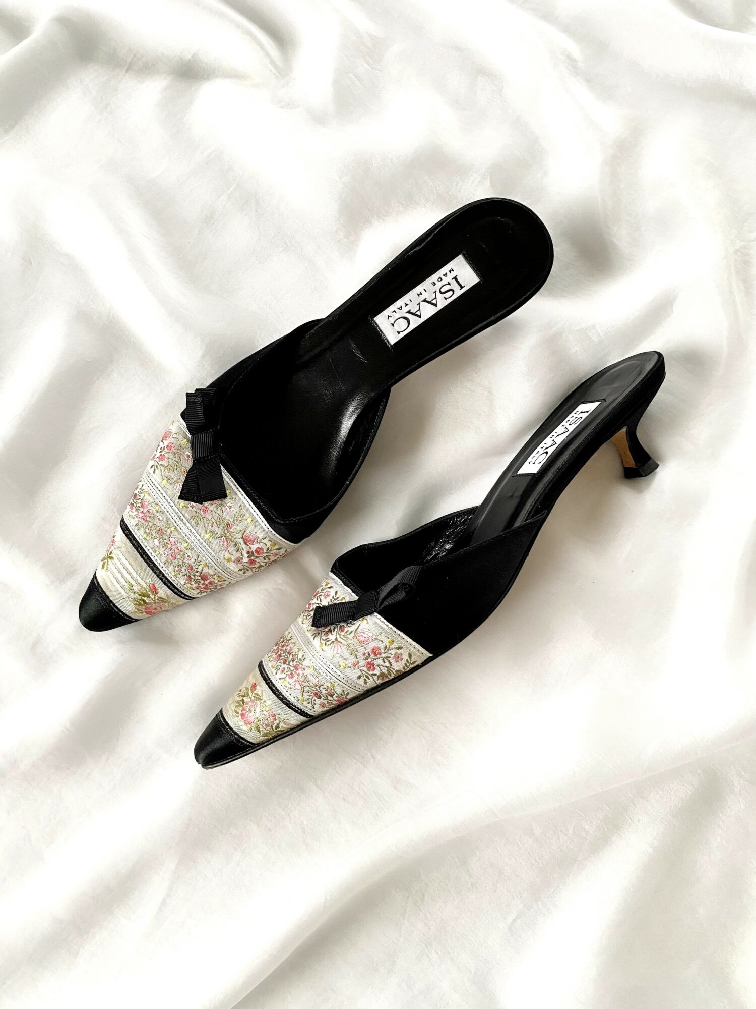 Pair of high-heeled shoes with black and patterned fabric, placed on white fabric background.