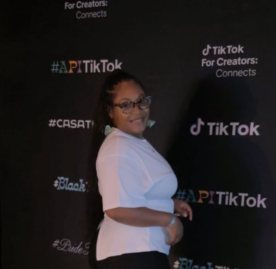 Person with glasses smiling, standing in front of a black backdrop with TikTok and event logos.