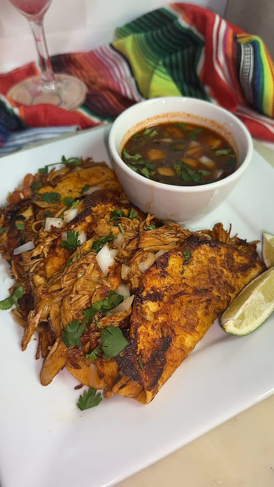 Plate with grilled fish, a bowl of sauce, and a lemon wedge, with colorful fabric in the background.