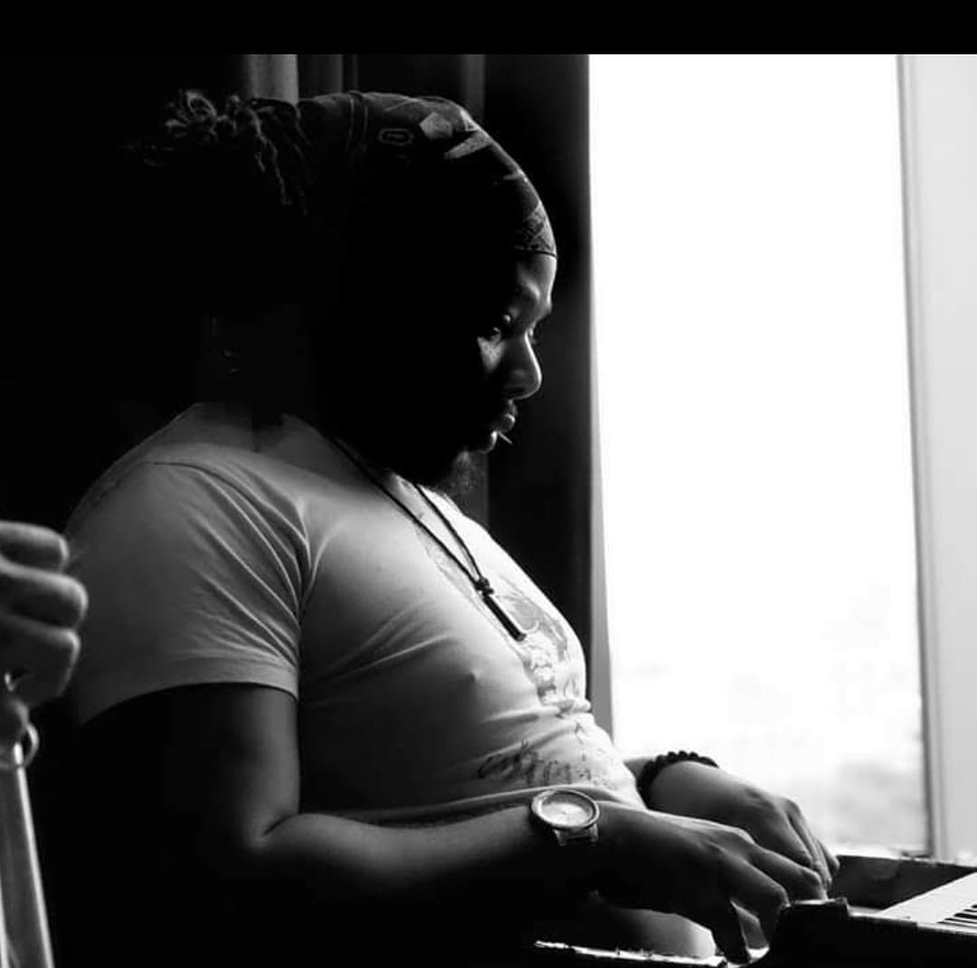 Woman sitting by window, looking down, with natural light illuminating her profile, wearing a headscarf and casual clothing.