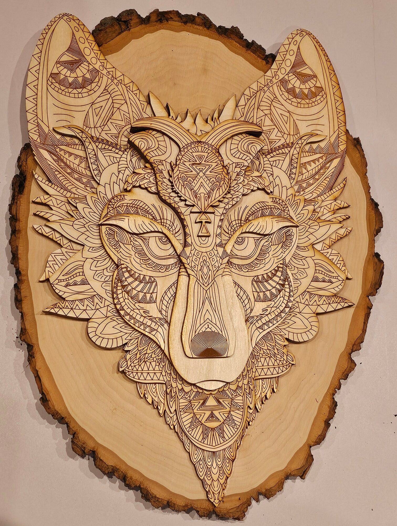 Intricate wood carving of a wolf's face with detailed patterns on a wooden slab background.