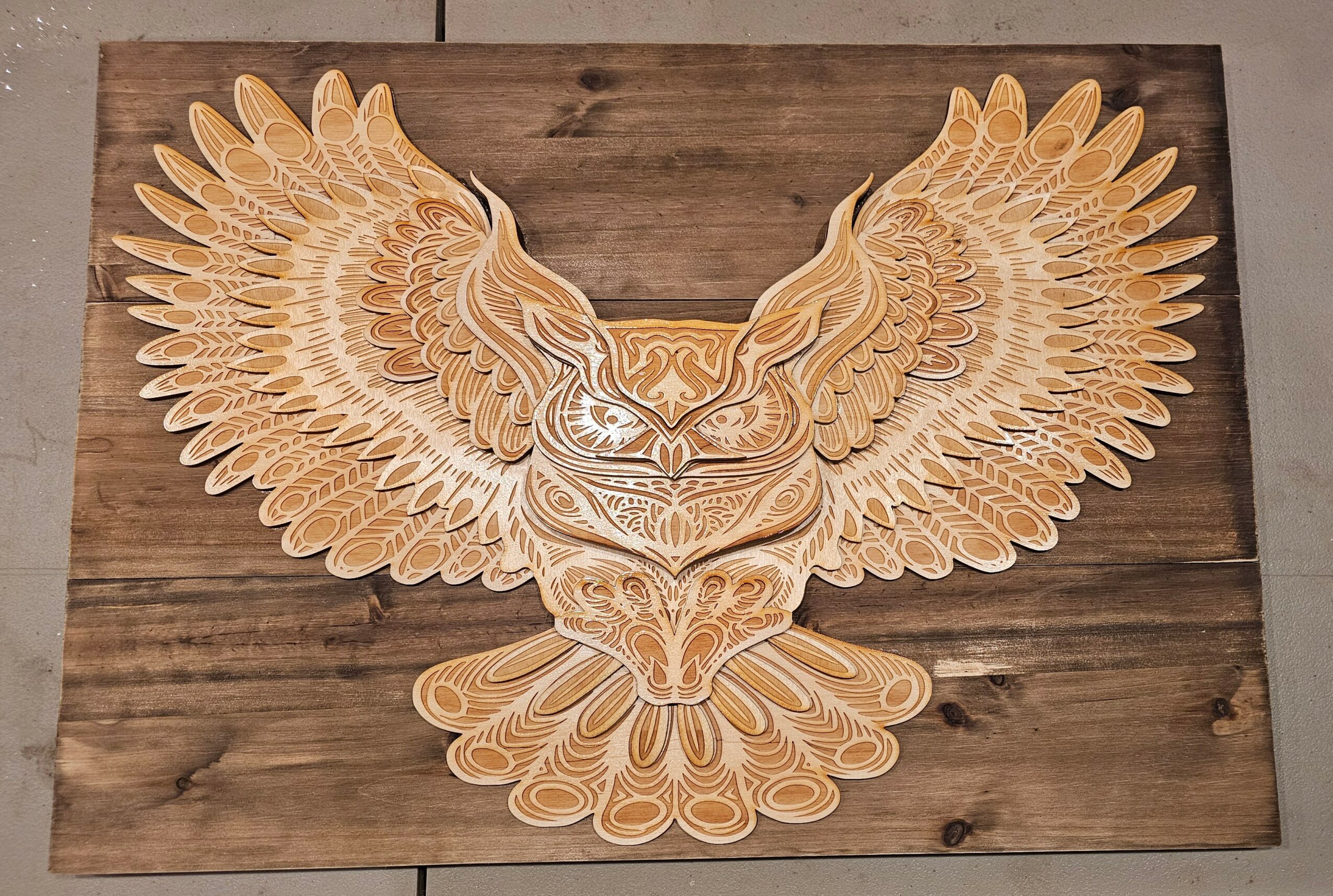 Wooden owl with outstretched wings mounted on a wooden background, detailed feather carvings, symmetrical design.