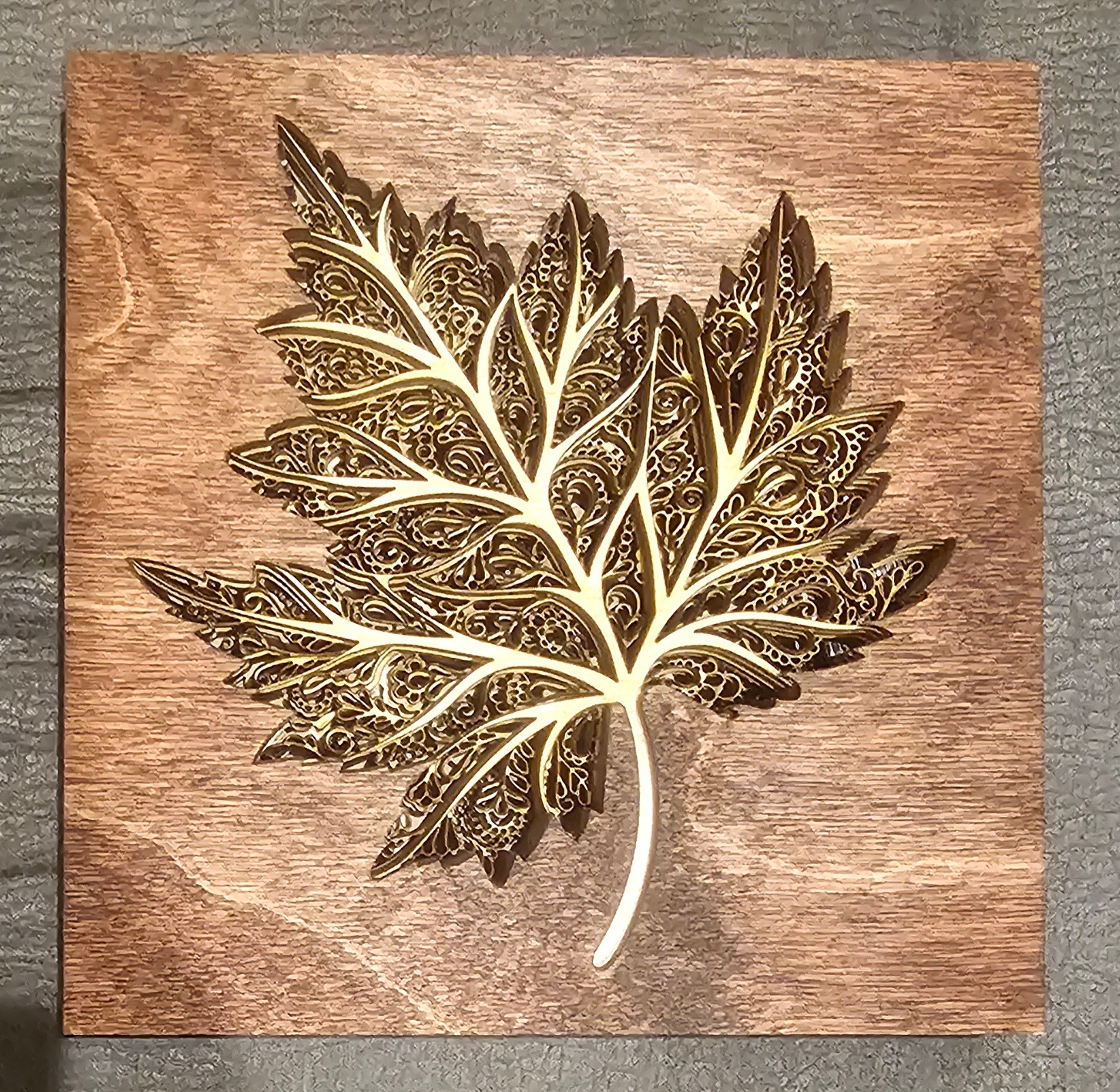 Decorative leaf-shaped wooden art piece on a wooden background, intricate design with cut-out details.
