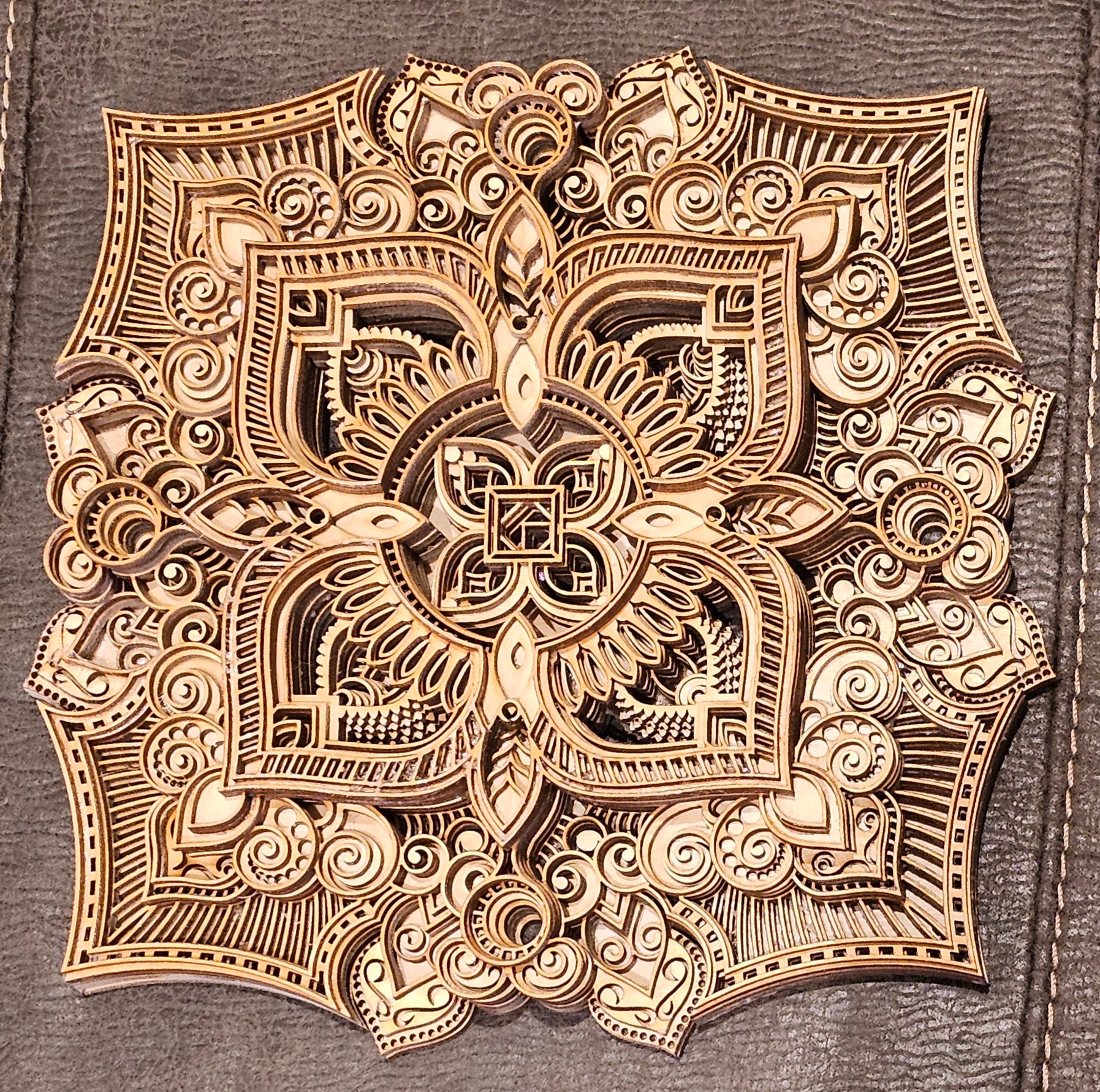 Intricate wooden mandala with detailed patterns and symmetrical design on a textured background.
