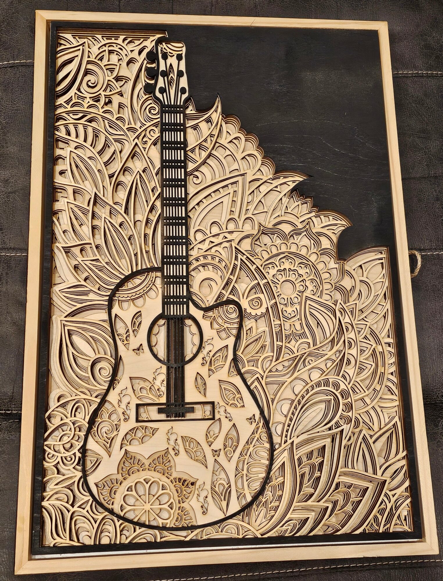 Intricate carved wooden artwork of a guitar with detailed patterns and designs, framed and displayed on a dark background.