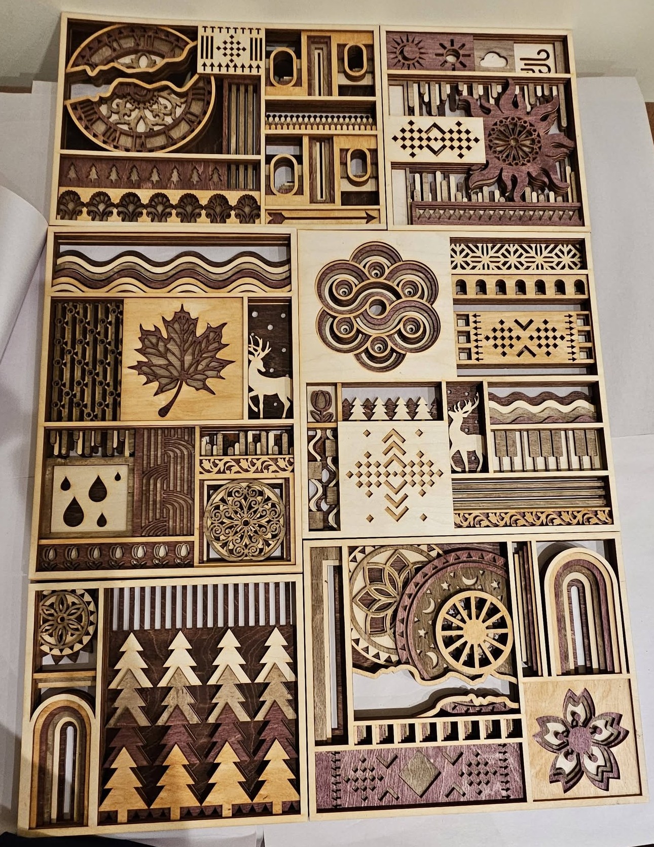 Collection of wooden boxes with various patterns, designs, and decorative items arranged in a grid, some with leaves, rain, and geometric shapes.
