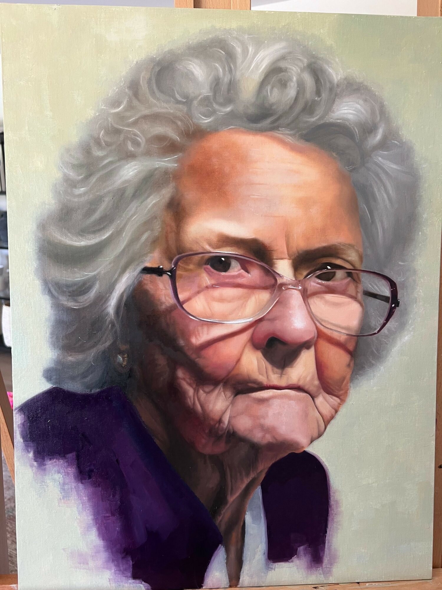 Portrait of an elderly woman with curly gray hair, glasses, and a purple top, smiling gently.