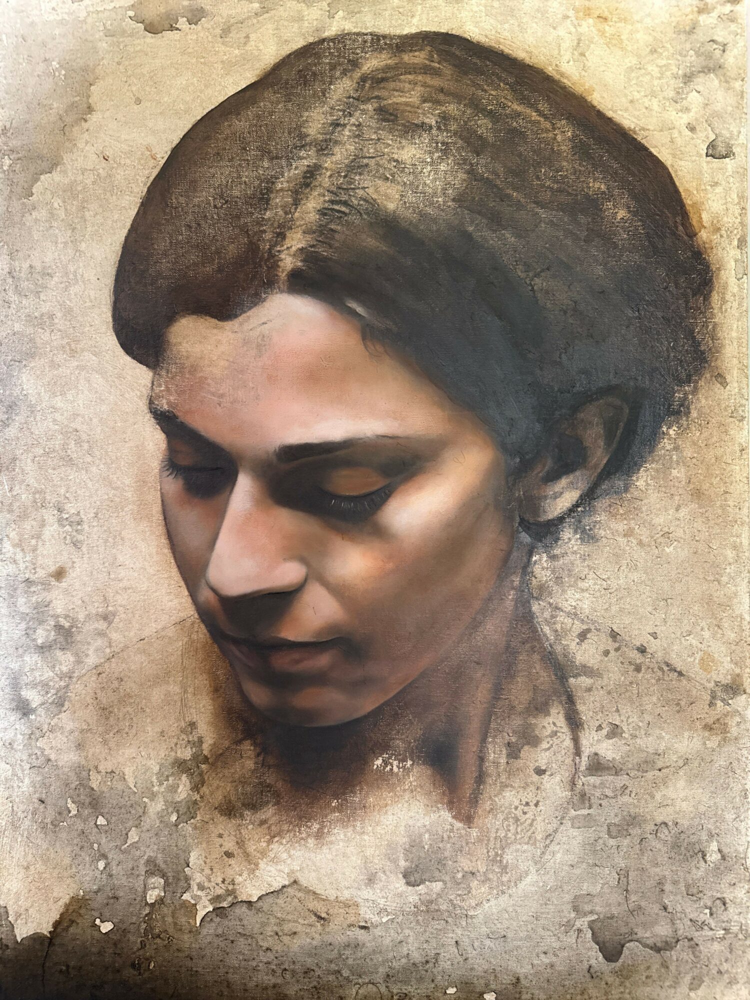 A realistic sculpture of a woman's head lying on a textured surface, with closed eyes and detailed facial features.