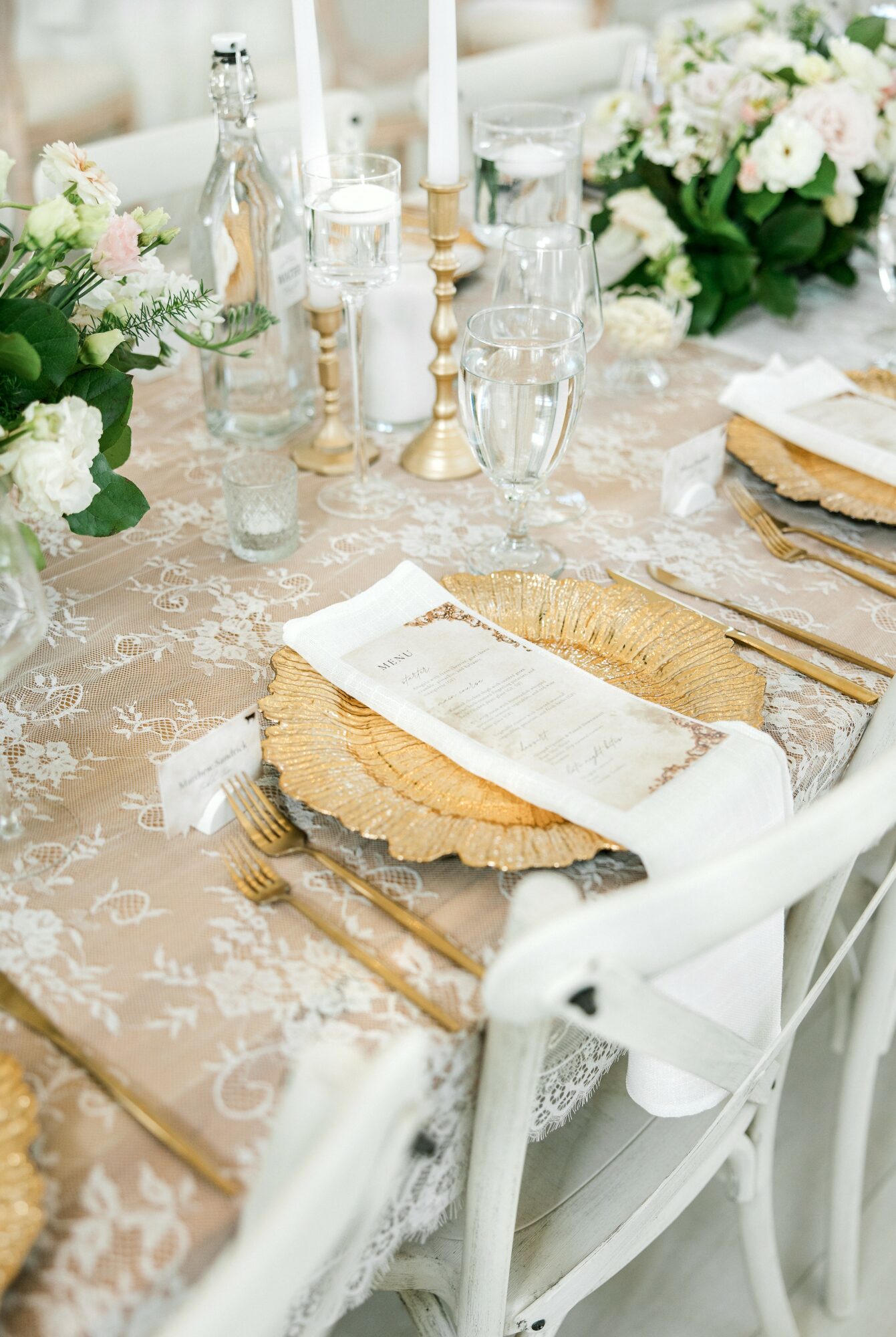 Table setting with floral arrangements, candles, glasses, and a napkin on a wooden charger plate, decorated for a celebration.