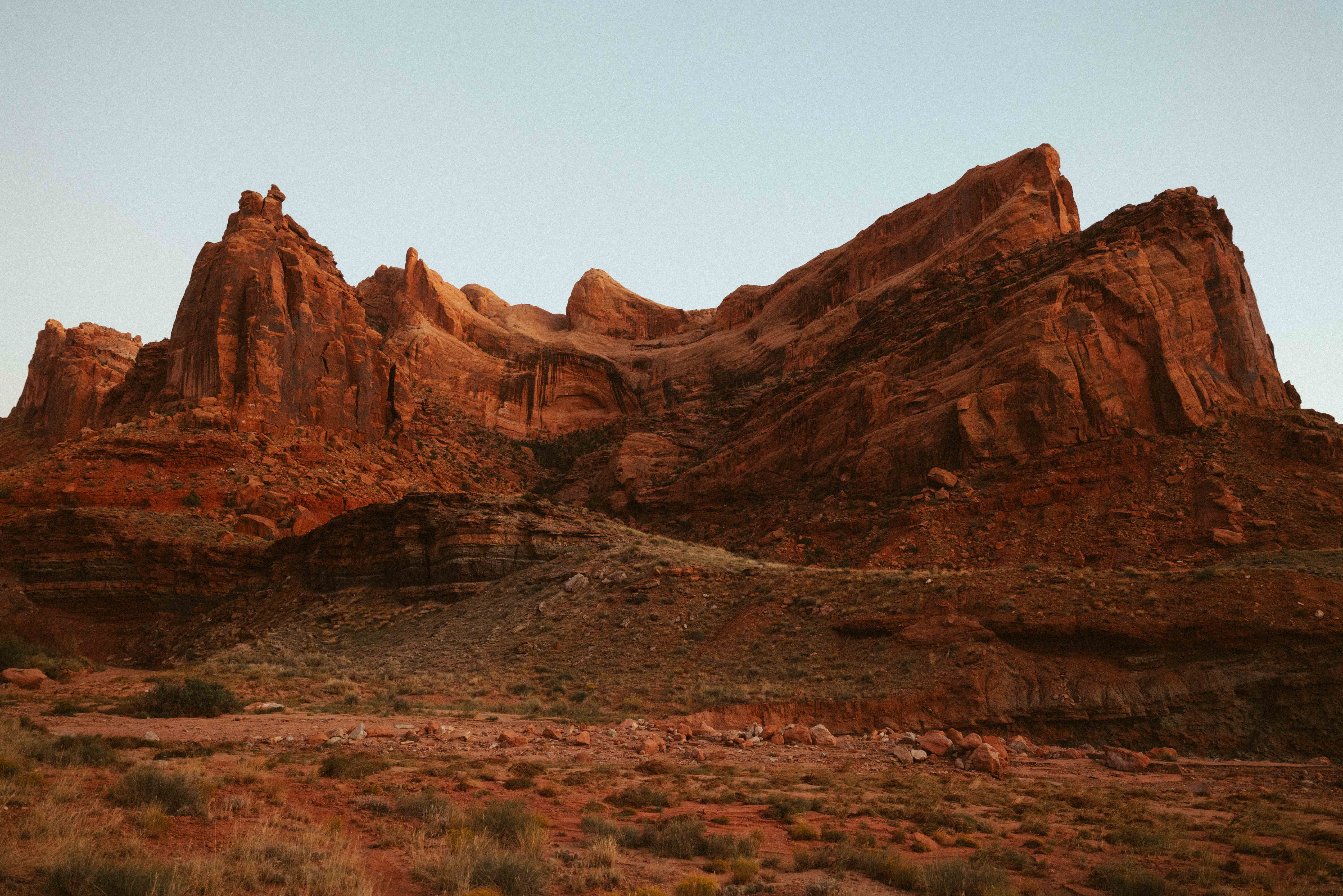 Red rock formations in a desert landscape with a clear sky, showing layered cliffs and rugged terrain.