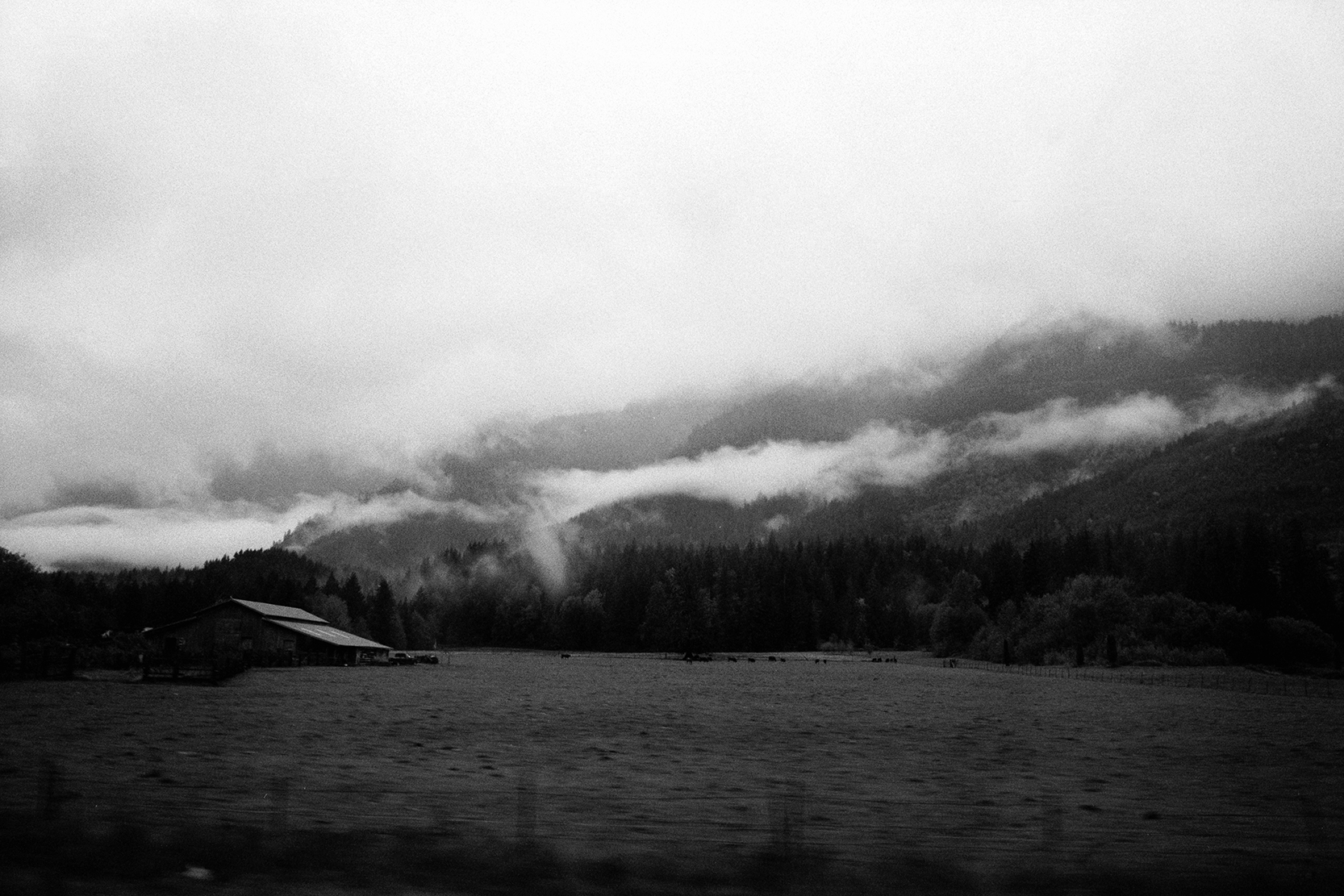 Landscape with cloudy sky over mountains and a field in the foreground, black and white image.