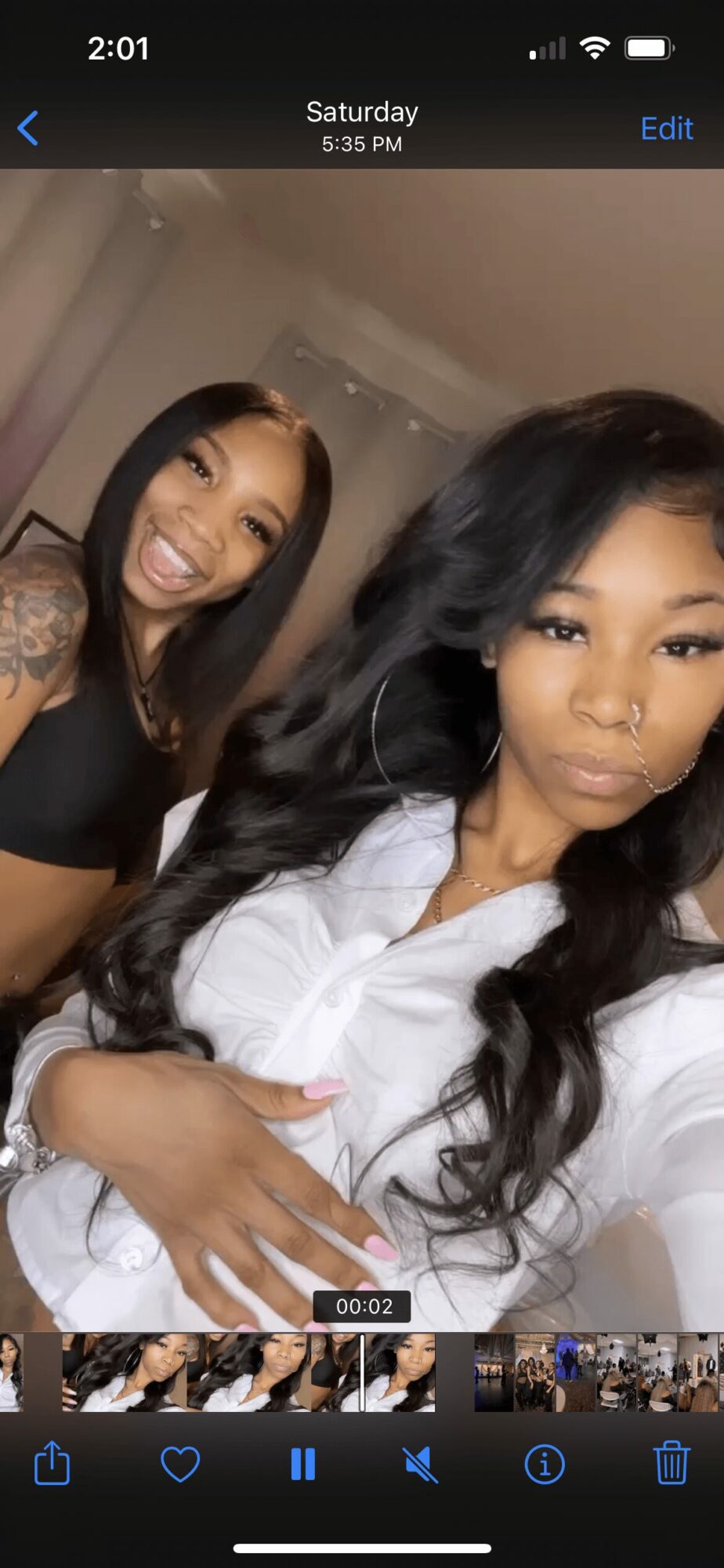 Two women taking a selfie indoors, one smiling with long dark hair, the other with long dark hair and a serious expression.