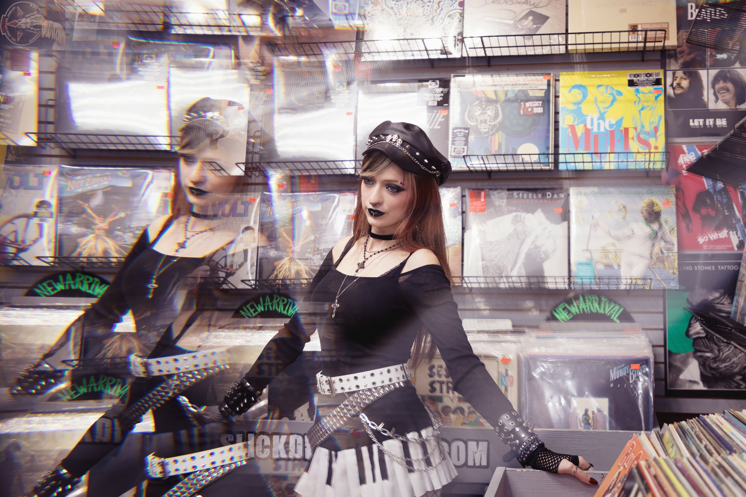 Two women in black outfits and hats pose in front of a display of vinyl records, with multiple album covers visible behind them.
